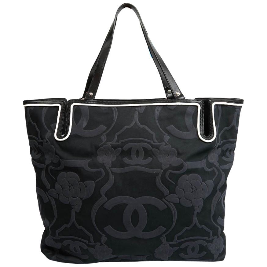Large tote or shopping bag from Maison Chanel in embossed canvas with black and anthracite gray background. In very good shape. The interior is lined in black fabric with several pockets, one of which is zipped. The rivets are in silver metal with