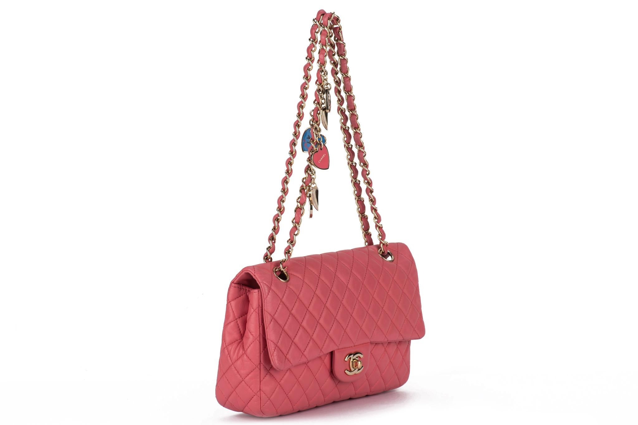 The Chanel Camellia charm classic single flap shoulder bag features a pink lambskin and a charmed chain. The bag features a leather-threaded polished gold chain-link shoulder strap, a rear patch pocket, and a matching gold classic CC turn-lock. An