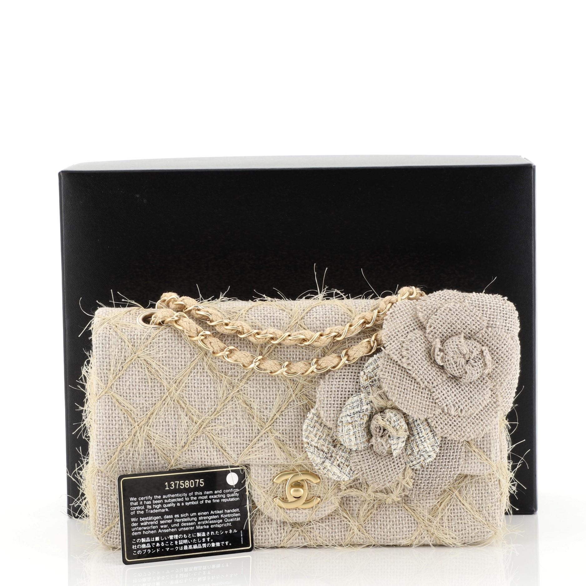 This Chanel Camellia Classic Single Flap Bag Quilted Burlap Medium, crafted from neutral quilted burlap, features quilted straw strands, woven-in chain link strap, exterior back pocket, burlap camellia applique details, and matte gold-tone hardware.