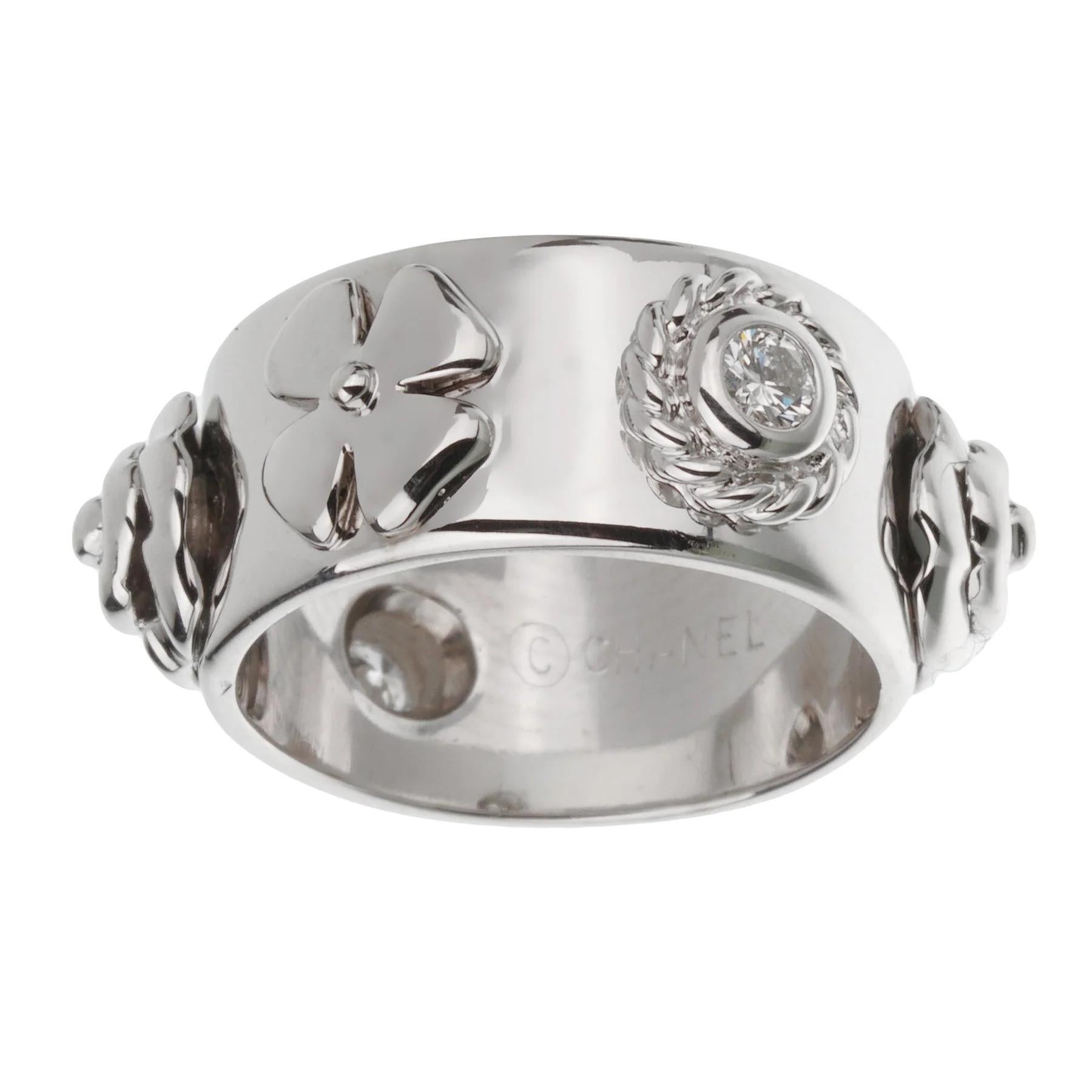 Il cinturino misura 5 1/2 e offre una presenza elegante ma sostanziale sul dito. La sua audace superficie in oro bianco lucido funge da tela perfetta per una serie di abbellimenti meticolosamente realizzati. Al centro del design c'è l'iconico fiore
