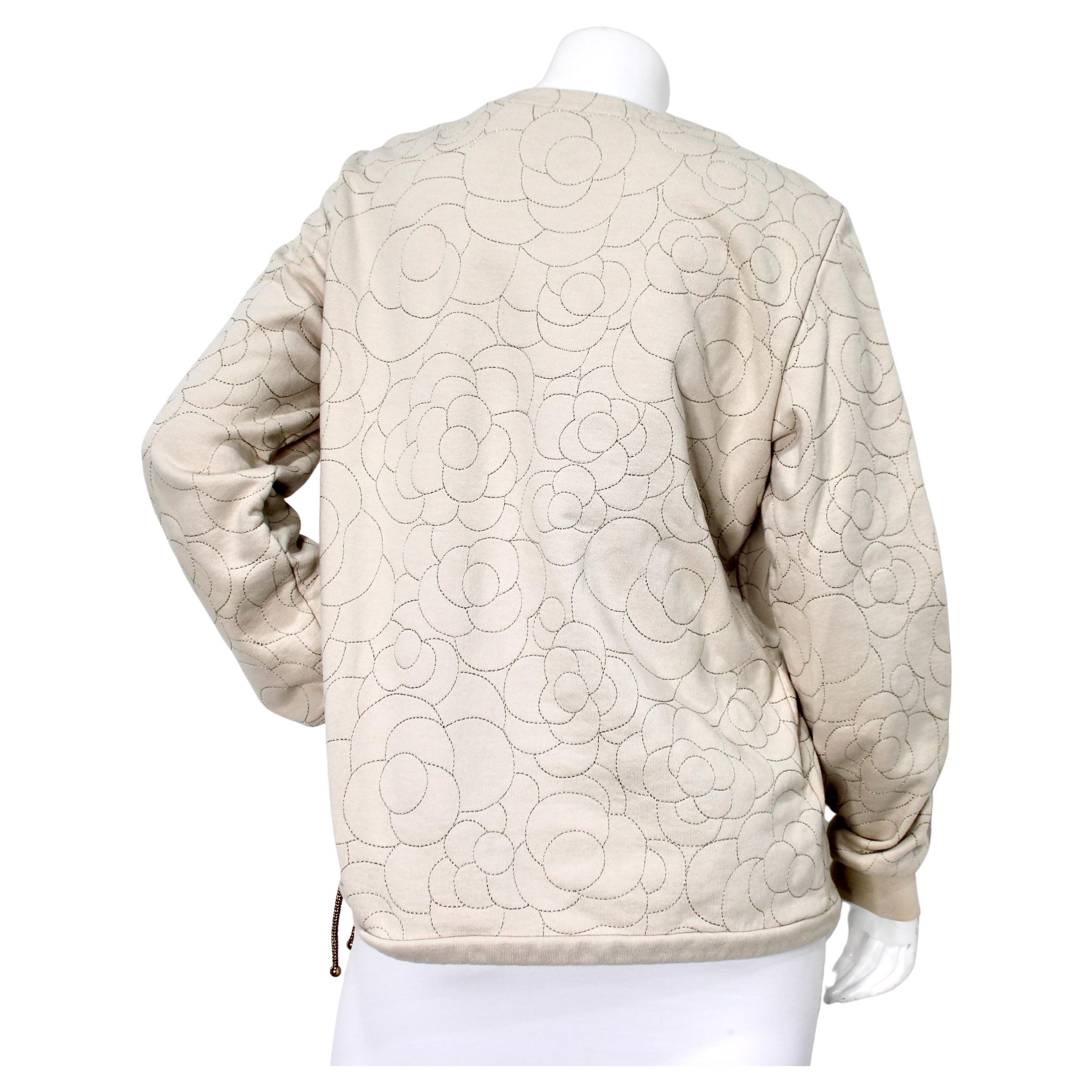 Le sweat-shirt à col ras du cou en coton beige surpiqué Chanel circa 2018 illustre l'élégance intemporelle avec une touche contemporaine. Confectionné en coton beige doux, ce luxueux sweat-shirt présente d'exquises surpiqûres dorées dans de délicats