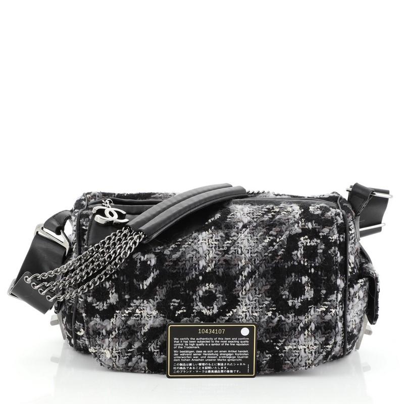 This Chanel Camera Bag Camellia Tweed and Leather Small, crafted in gray tweed and black leather, features camellia design, chain shoulder strap with leather, exterior side pockets and gunmetal-tone hardware. Its zip closure opens to a black fabric