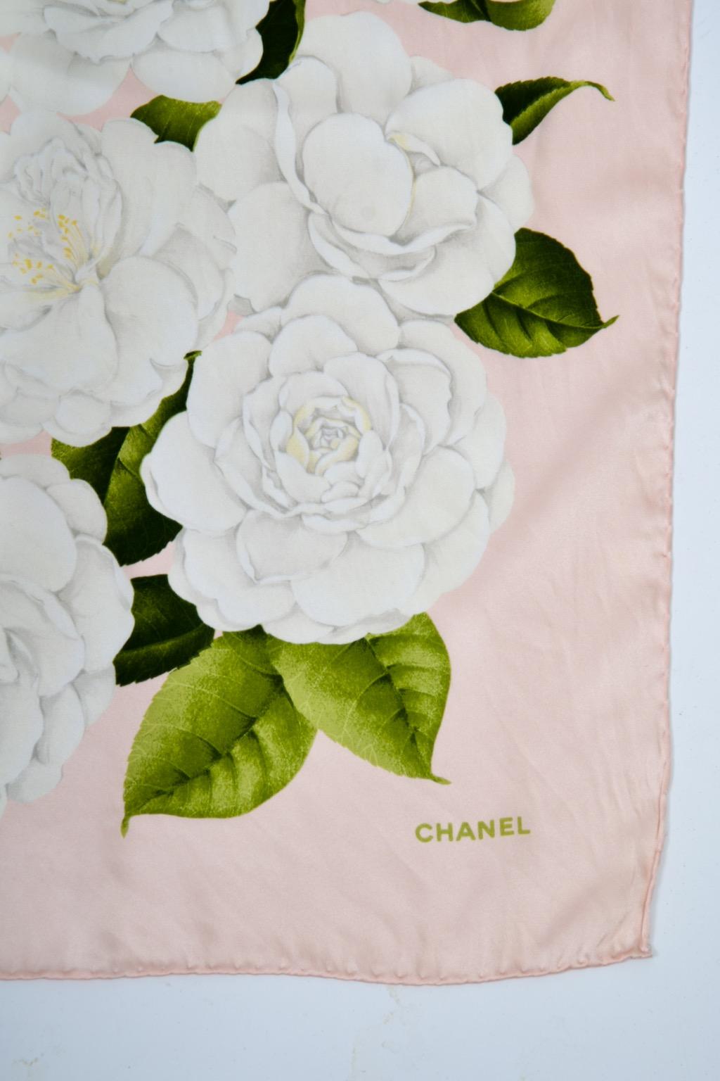 Pañuelo Chanel vintage de seda con camelias, con un fondo rosa pálido salpicado de camelias blancas y acentuado con hojas verdes. Chanel impreso en mayúsculas verdes en la parte inferior derecha. Bordes enrollados a mano. 35