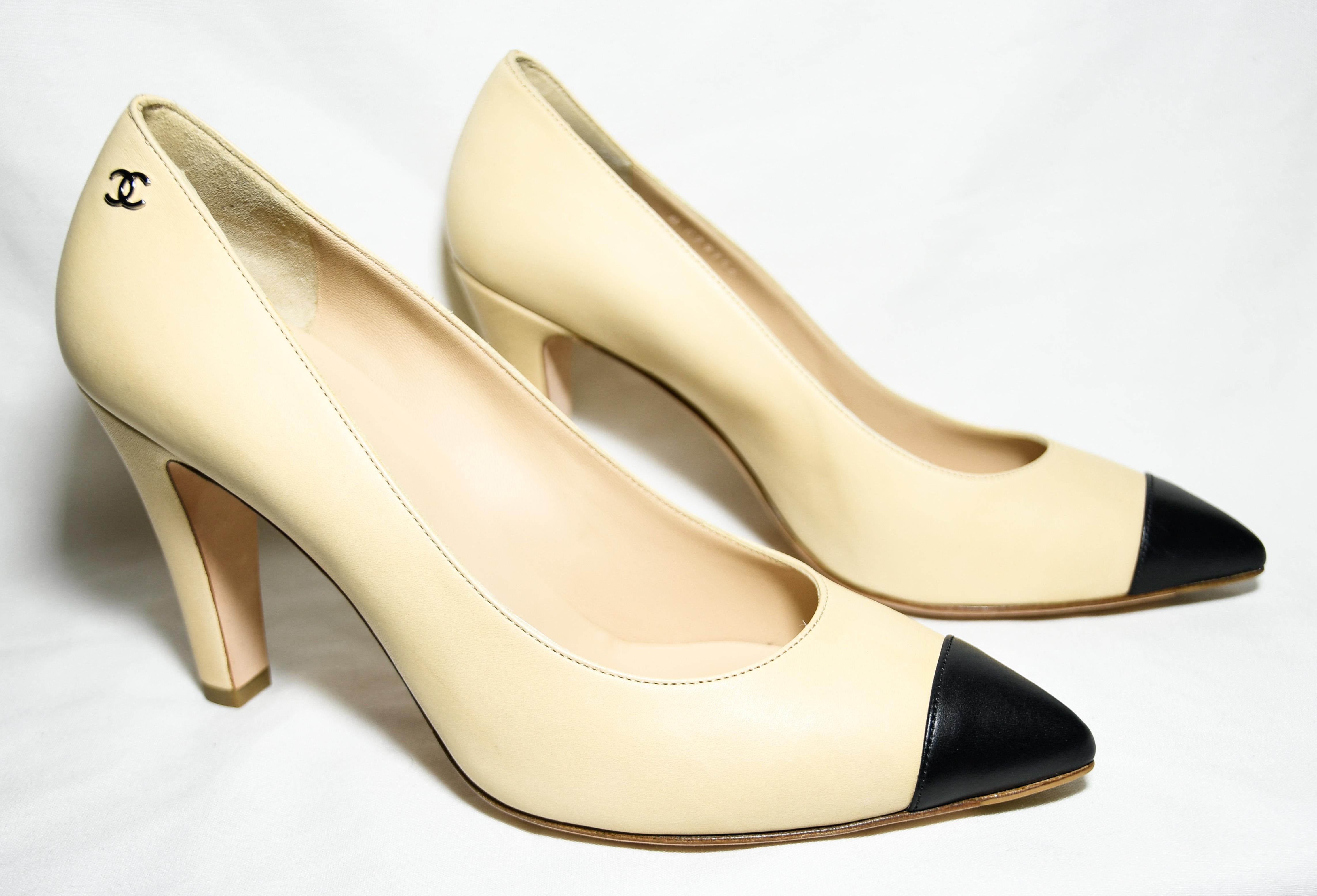 Chanel cap toe in black on beige leather pumps that include gold tone metal CC on the top side of heel.   Beige and black matte leather Chanel pumps with covered heels and are lined in beige leather.  These shoes are in excellent condition.  Heel 4