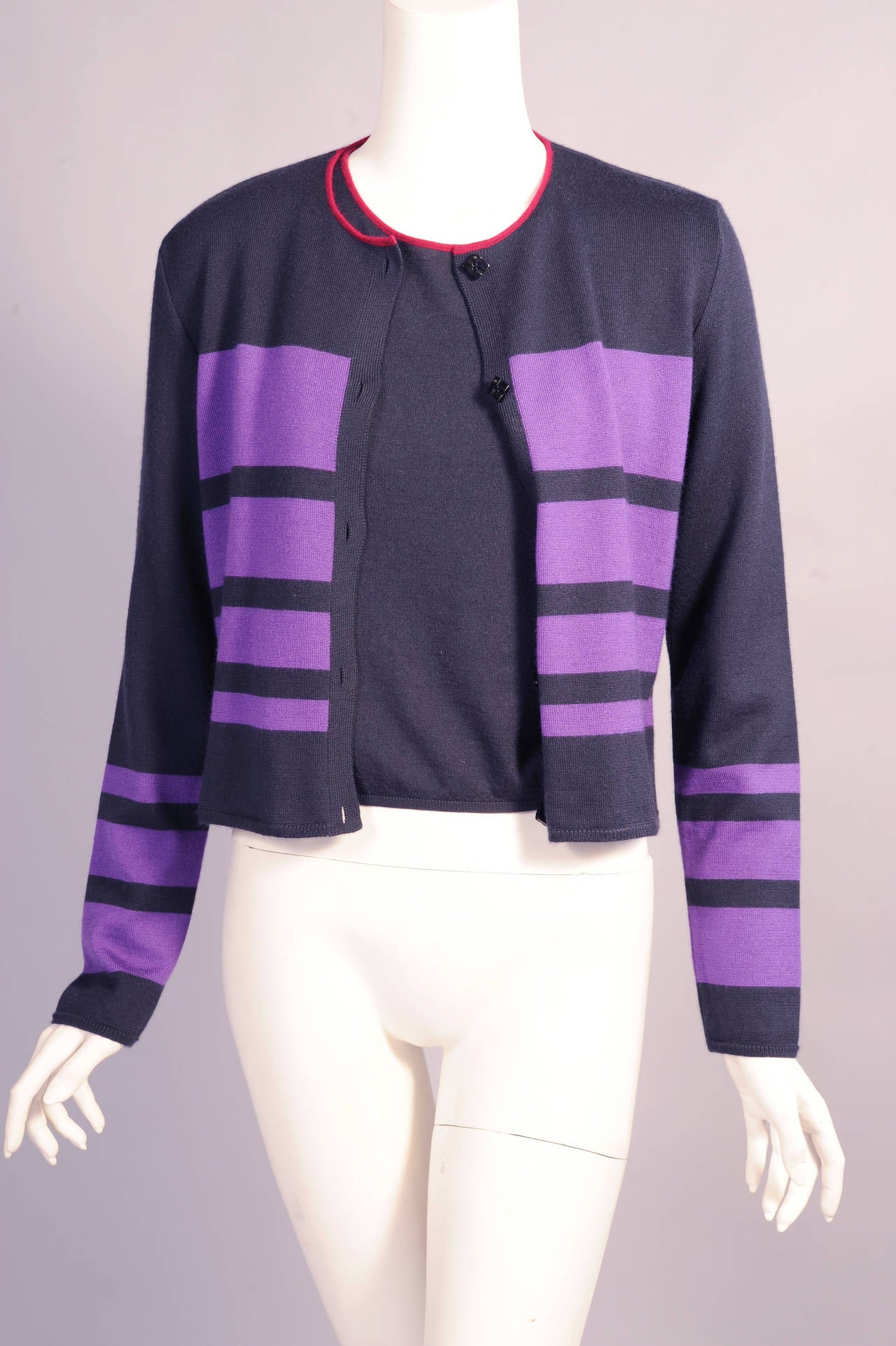 A midnight blue cashmere and silk blend cardigan has a burgundy edge at the neckline and purple bands in decreasing widths on the body. There are five black Chanel logo buttons at the center front. A midnight blue sleeveless sweater with a matching