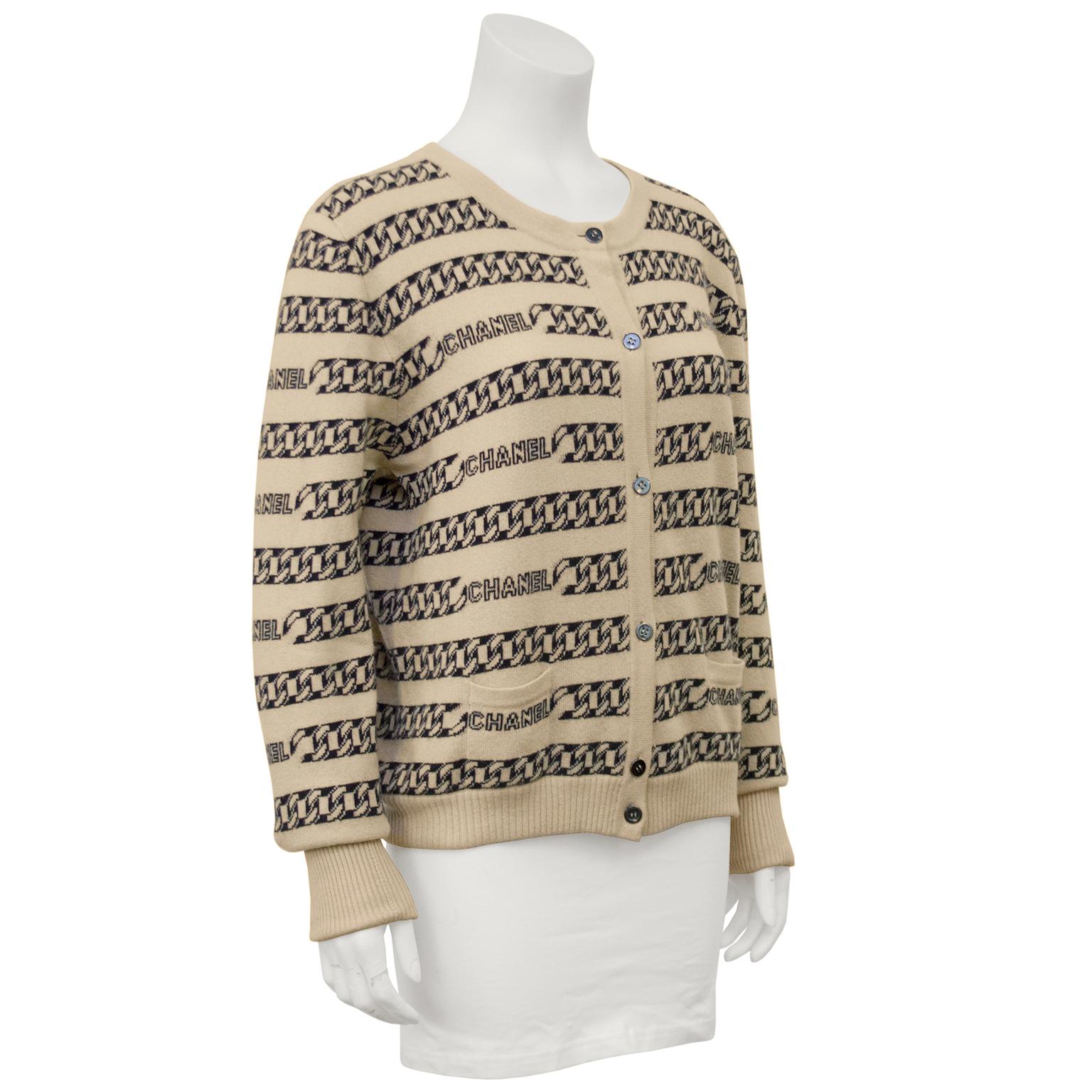 Beige and black classic colored Chanel cashmere cardigan from the 2001 Autumn collection. Chain style intarsia CC logo throughout the body of the sweater interspersed with CHANEL branded wording. Two front pockets and button front. In excellent