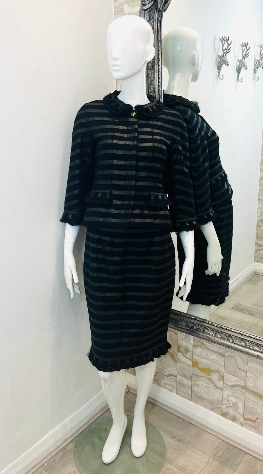 Chanel Cashmere Skirt & Jacket Suit

Black suit designed with dark silver, horizontal stripe pattern and ruffle trim details.

Cropped jacket styled with three-quarter sleeves, collared neckline and gold 'CC' logo Eagle button.

Featuring hidden