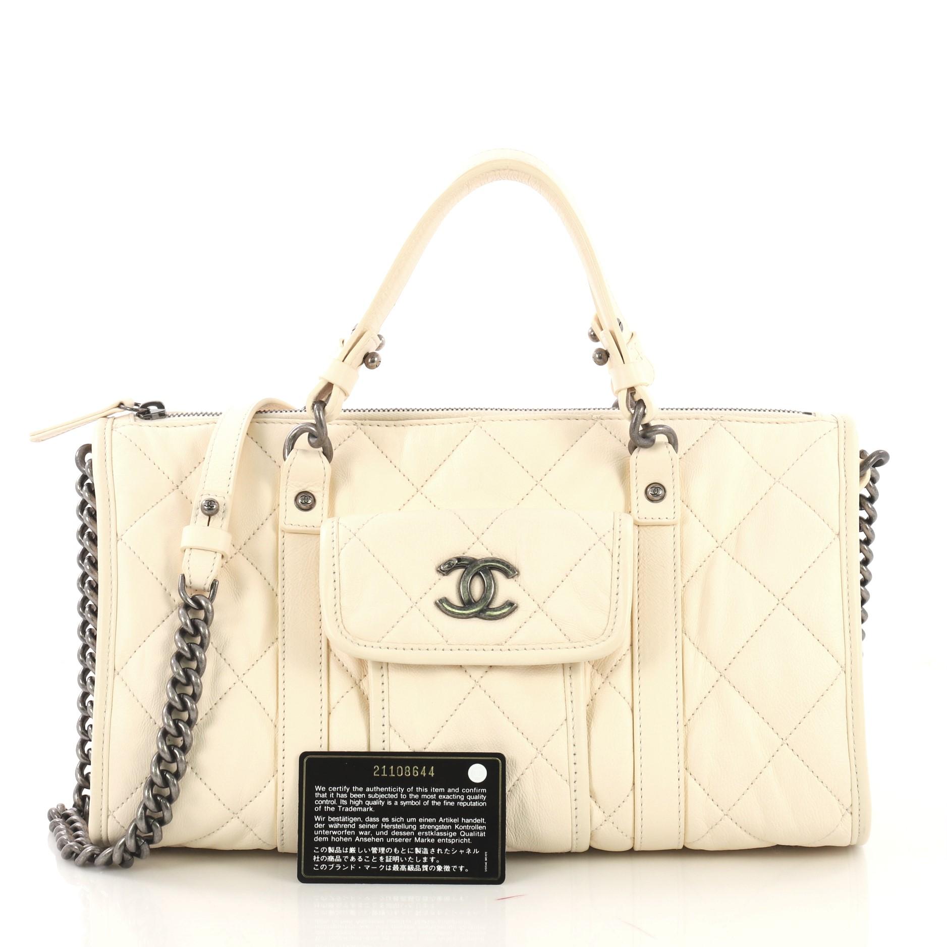 This Chanel Casual Riviera Bowling Bag Quilted Calfskin Medium, crafted from white quilted calfskin leather, features dual top leather handles, chain link strap with leather pad, exterior front pocket with CC logo, protective base studs and aged