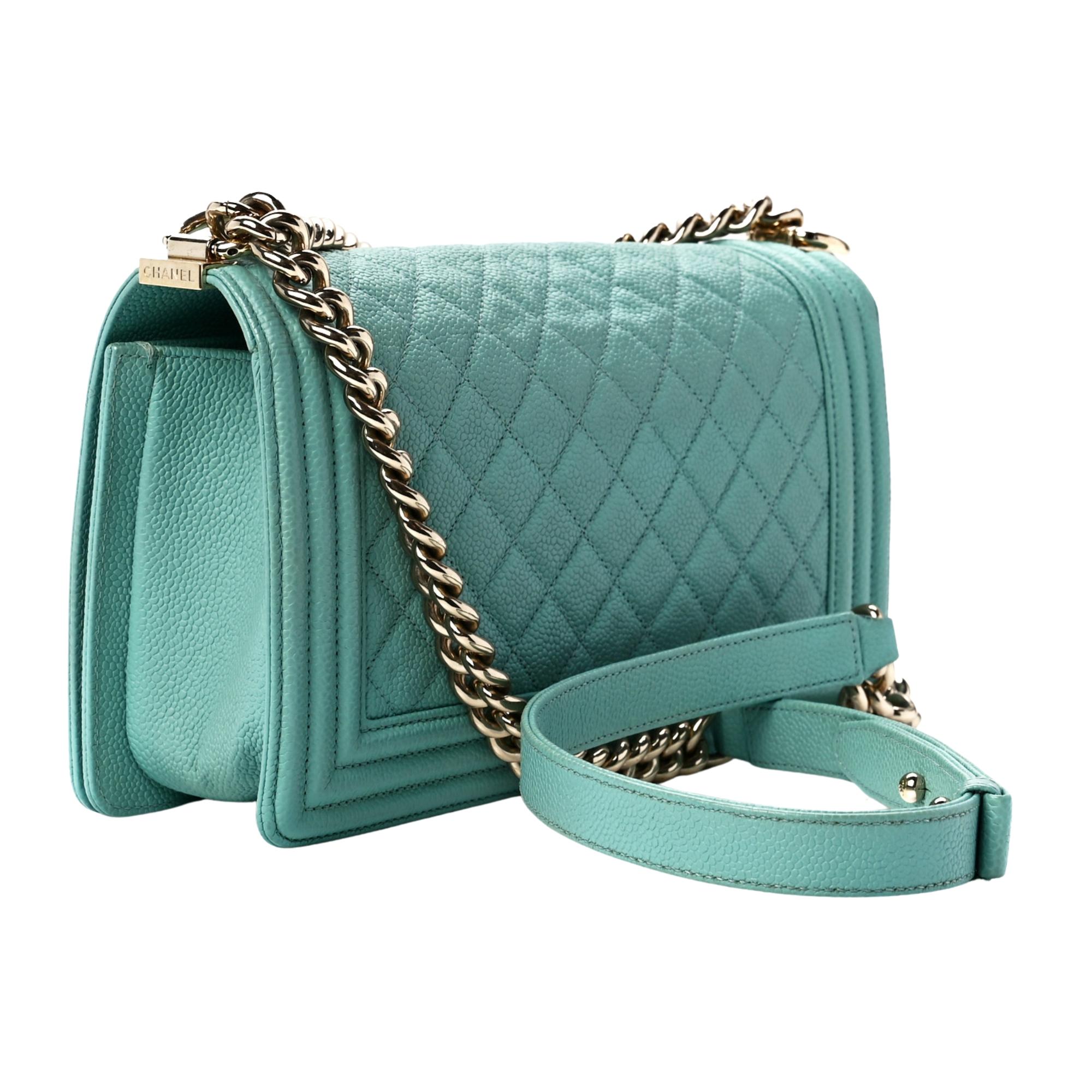 This bag is made of diamond quilted caviar leather in light blue with a structured rectangular silhouette. The bag features a polished light silver chain link shoulder strap with a leather shoulder pad, and a frontal unique squared polished gold Boy