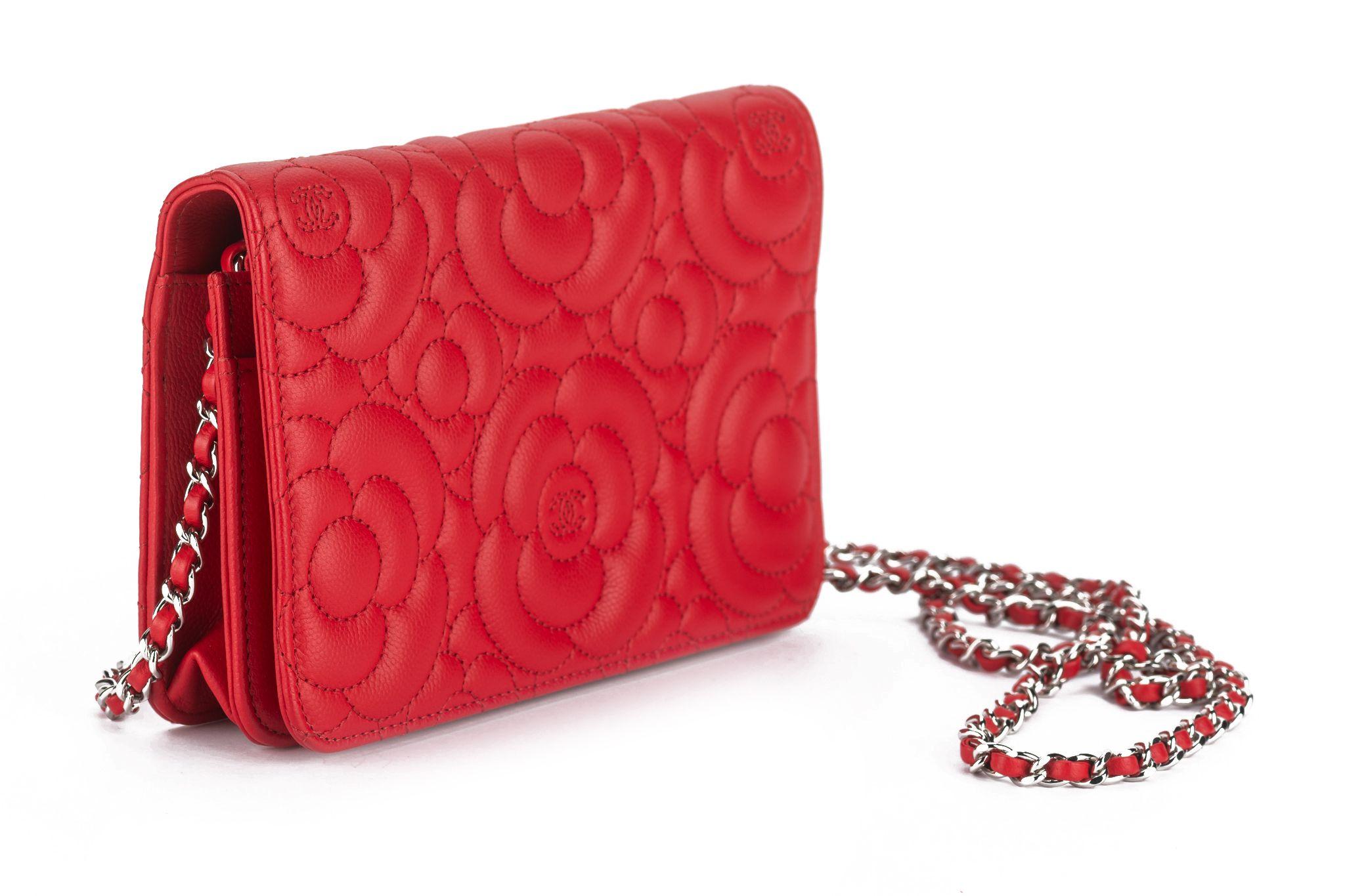 This Chanel Caviar Camellia embossed wallet on chain is in red. It is a classic, stylish clutch with finely crafted Camellia embossed quilted leather with a silver CC logo. The wallet features an extra-long gold chain link shoulder strap threaded