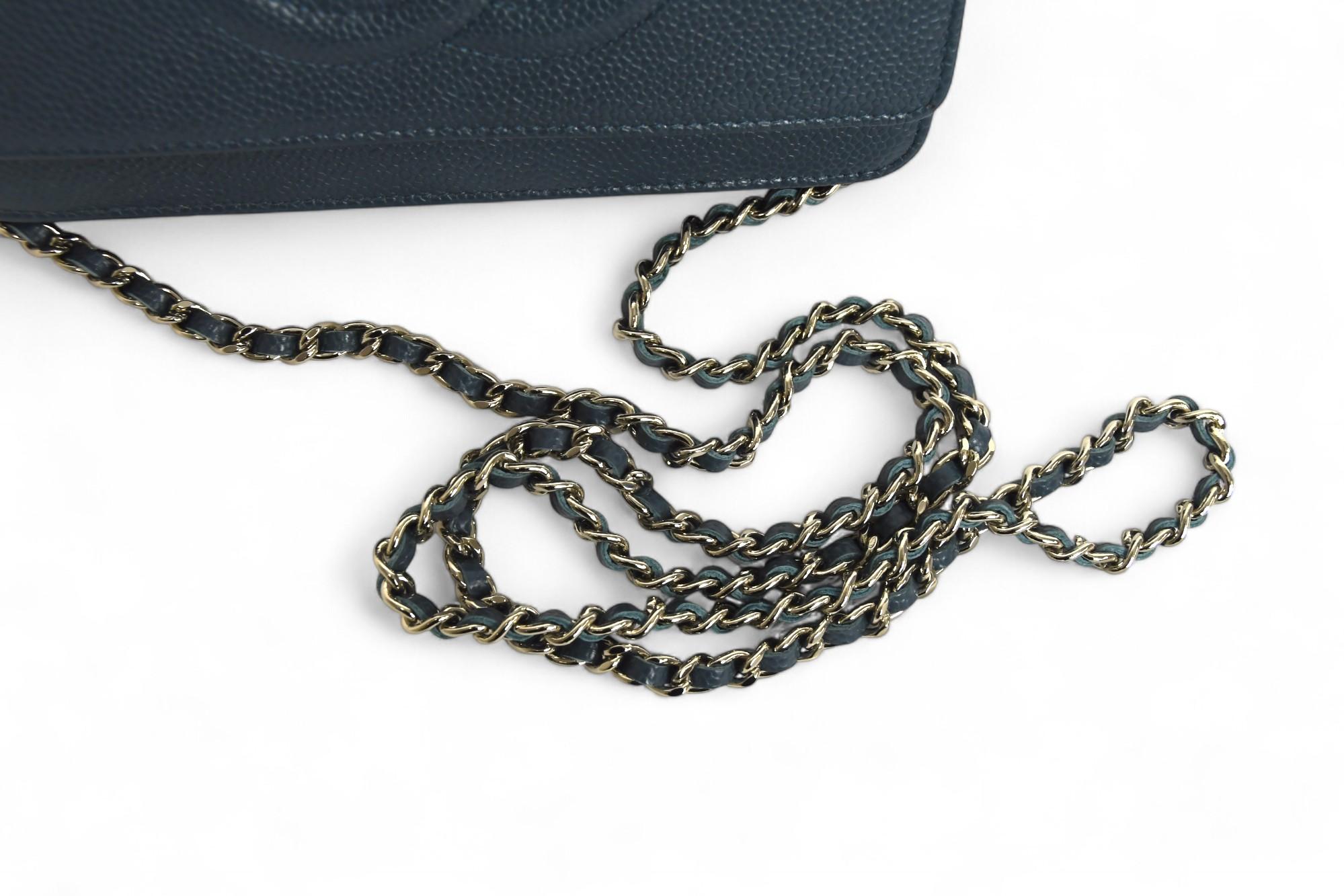 Dieses Chanel Portemonnaie an der Kette ist die perfekte Verbindung von Eleganz und Zweckmäßigkeit. Es ist aus strapazierfähigem, marineblauem Kaviarleder mit feiner Kieselsteineffektstruktur gefertigt. Das kultige, ineinander greifende CC-Logo ist