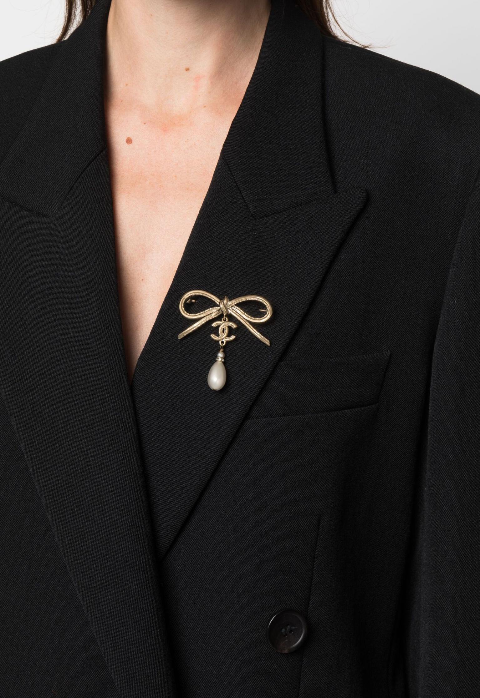 Chanel 2000er CC-Brosche mit Schleife, goldfarbenem, ineinandergreifendem CC-Logo und goldfarbenem
Perlenverzierung, Schleifenverzierung, Tropfenform, Stangenverschluss und eine Logoplakette auf der Rückseite. 
Um die 2000er Jahre.
Guter