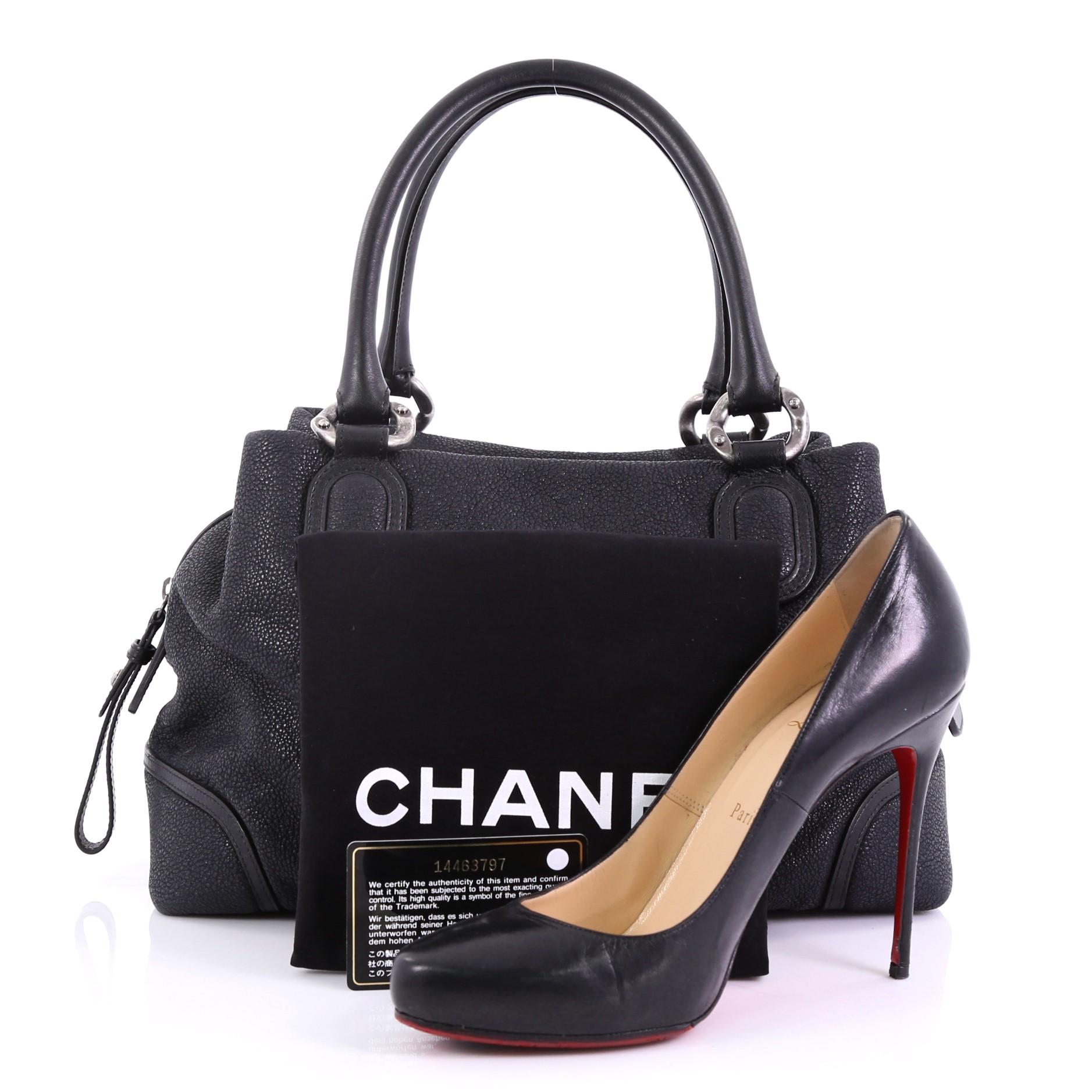 This Chanel CC Bowling Bag Iridescent Goatskin Medium, crafted in black iridescent goatskin, features dual rolled leather handles, Chanel CC logo on front, protective base studs, and aged silver-tone hardware. Its zip closure opens to a gray fabric