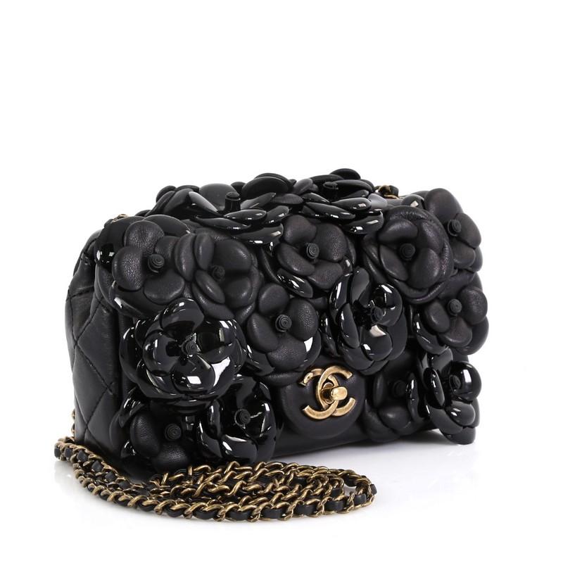 This Chanel CC Camellia Flap Bag Lambskin with Patent Mini, crafted in black leather embellished with hand stitched camellia black patent and leather flowers, features woven-in leather chain straps, CC turn-lock closure and aged gold-tone hardware.