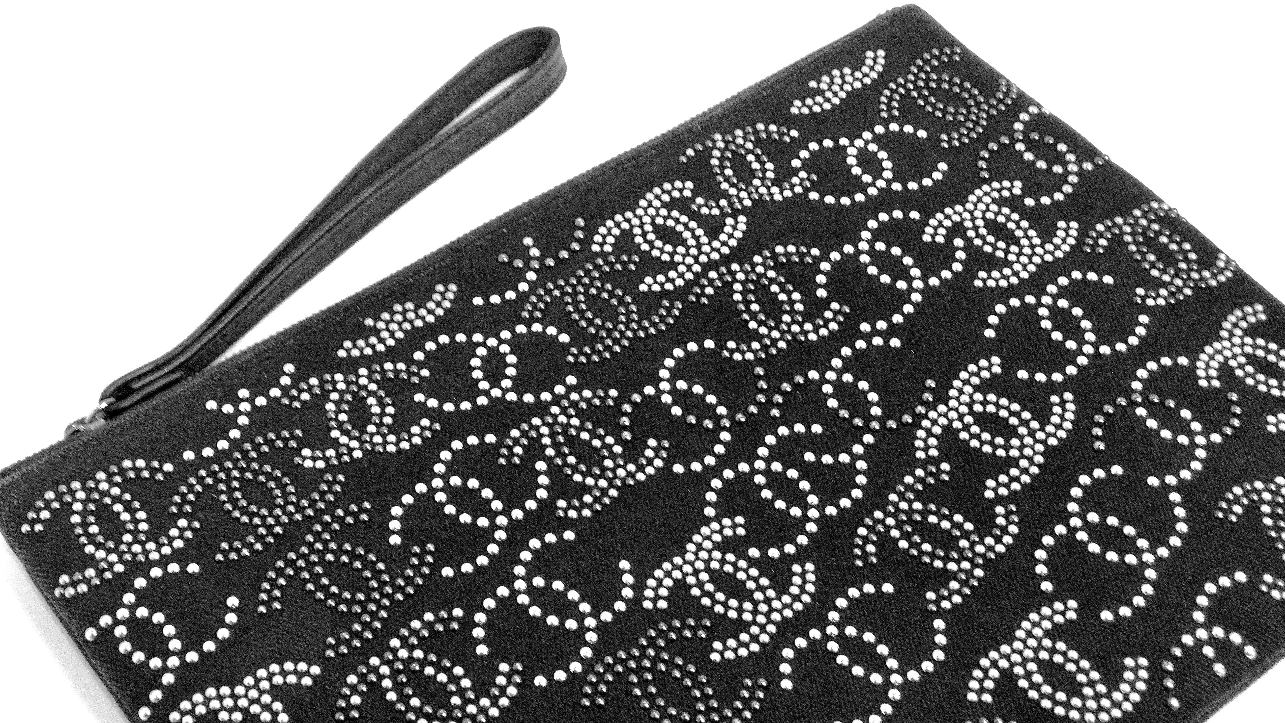 The Chanel CC Canvas Black Studded Pouch is a striking accessory that blends edgy style with glamorous flair. This chic pouch is adorned with silver rhinestone CC logos, with a large CC rhinestone logo on the back, creating a dazzling effect.