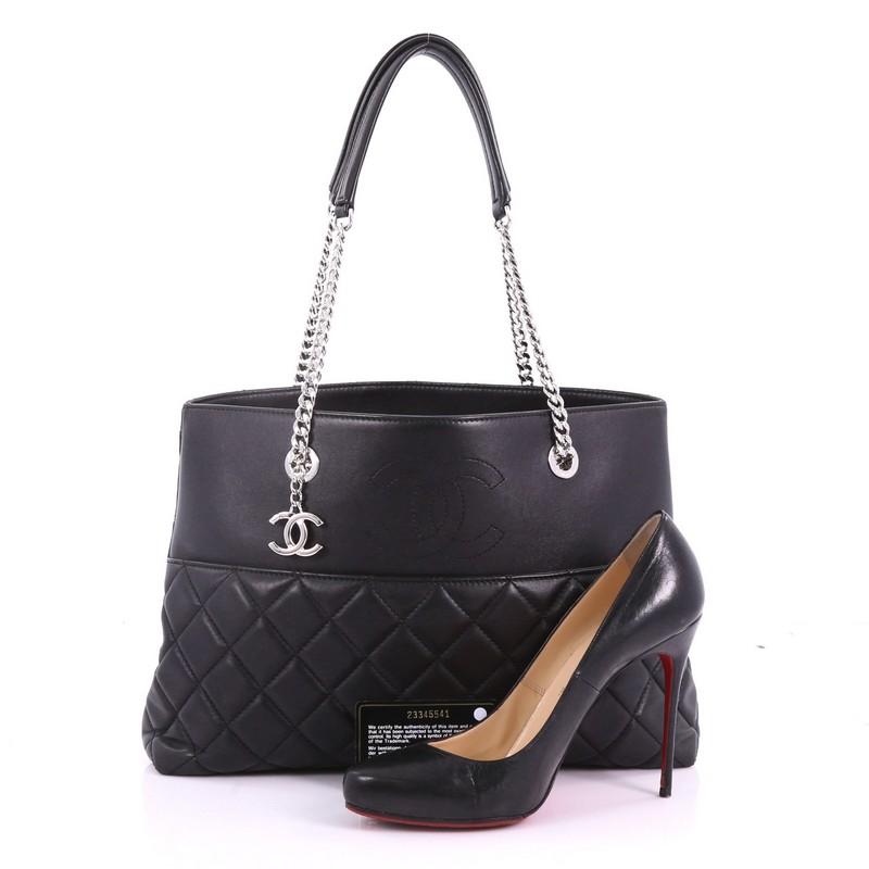 This Chanel CC Charm Open Shopping Tote Quilted Lambskin Large, crafted from black quilted lambskin leather, features dual chain-link shoulder strap with leather pads, exterior back pocket, and silver-tone hardware. Its wide open top showcases a