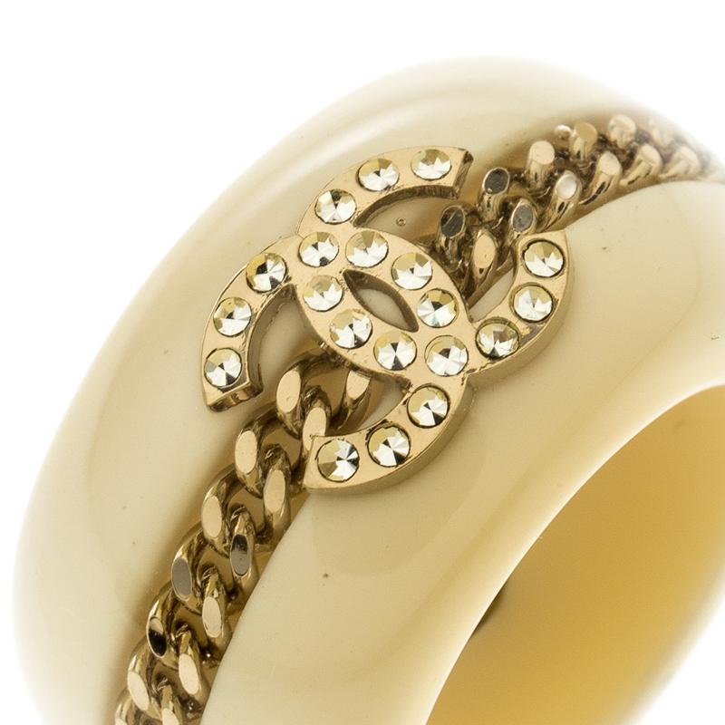 To give company to your french manicure nails and delicate fingers is this stunning ring from Chanel. The wide band ring is crafted from cream resin and features gold-tone metal chain and CC crystal embellishment detailng in the center. The interior