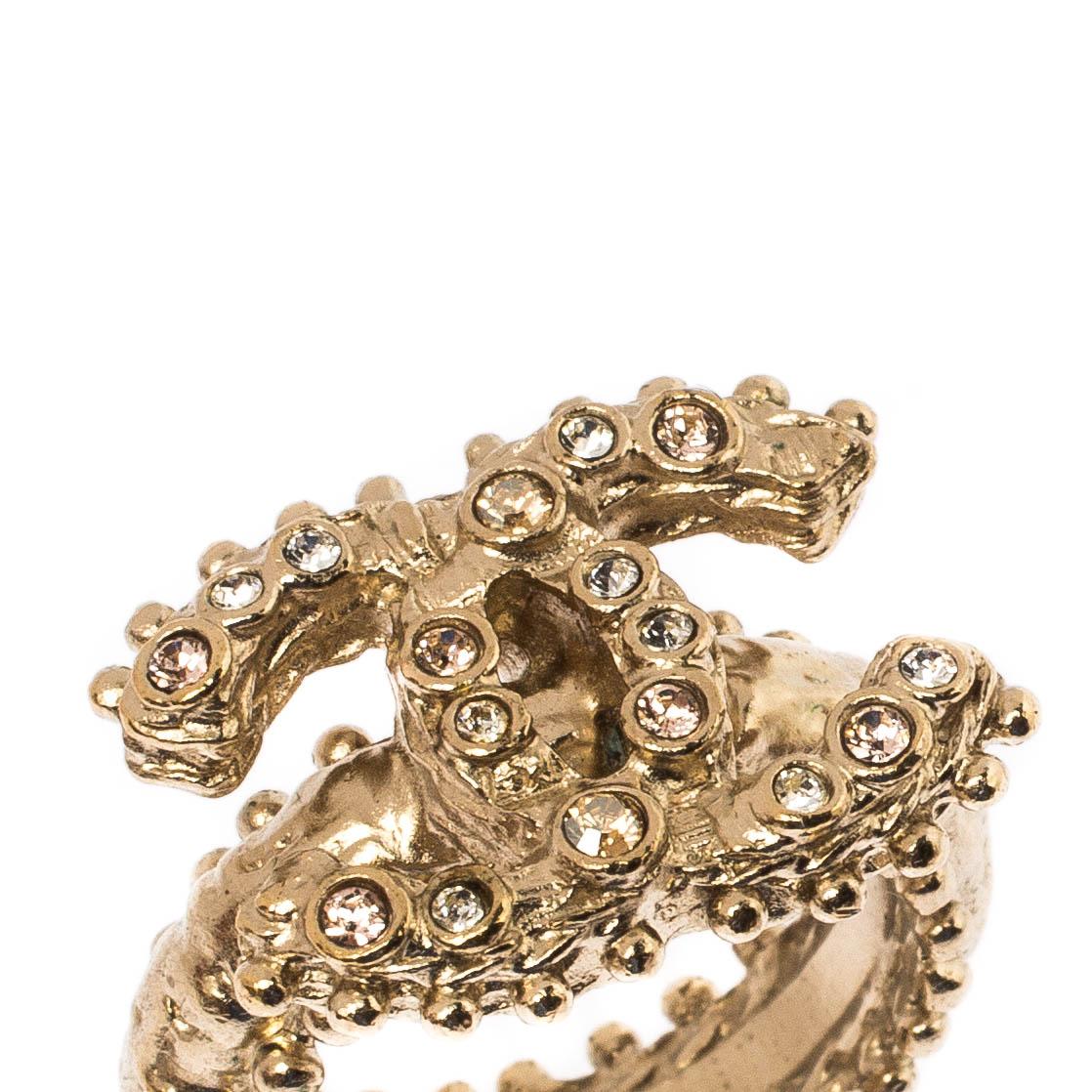 This exquisite ring by Chanel will make a timeless addition to your collection. Crafted from gold-tone metal, this gorgeous ring features the signature CC logo at the centre, detailed with crystals and the ring is given a textured finish. This