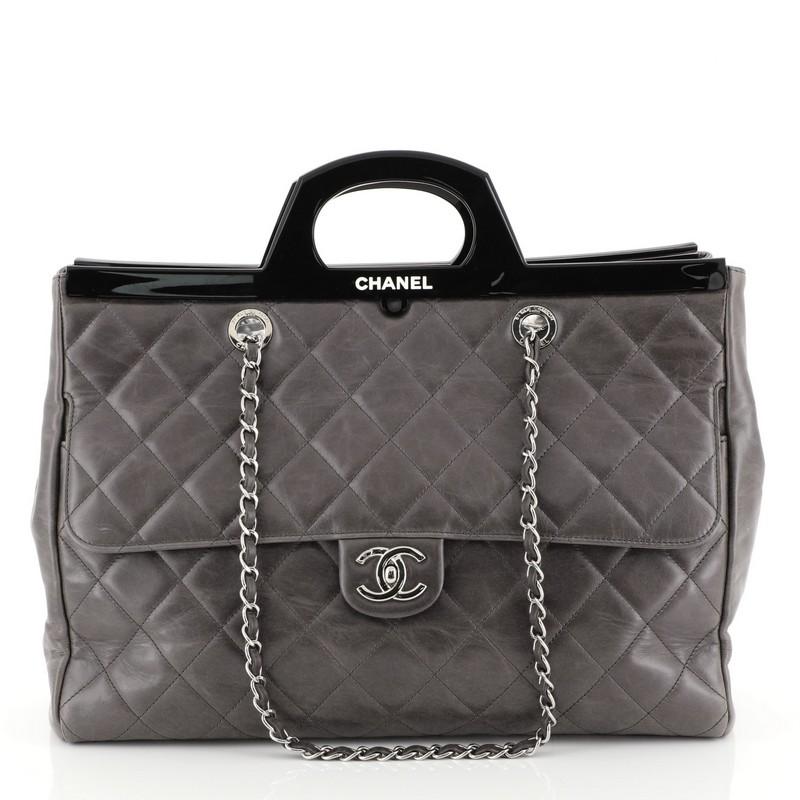 This Chanel CC Delivery Tote Quilted Glazed Calfskin Large, crafted from gray quilted glazed calfskin leather, features woven-in leather chain link straps, exterior back slip pocket, top lacquer shaped top handles, front flap compartment with CC