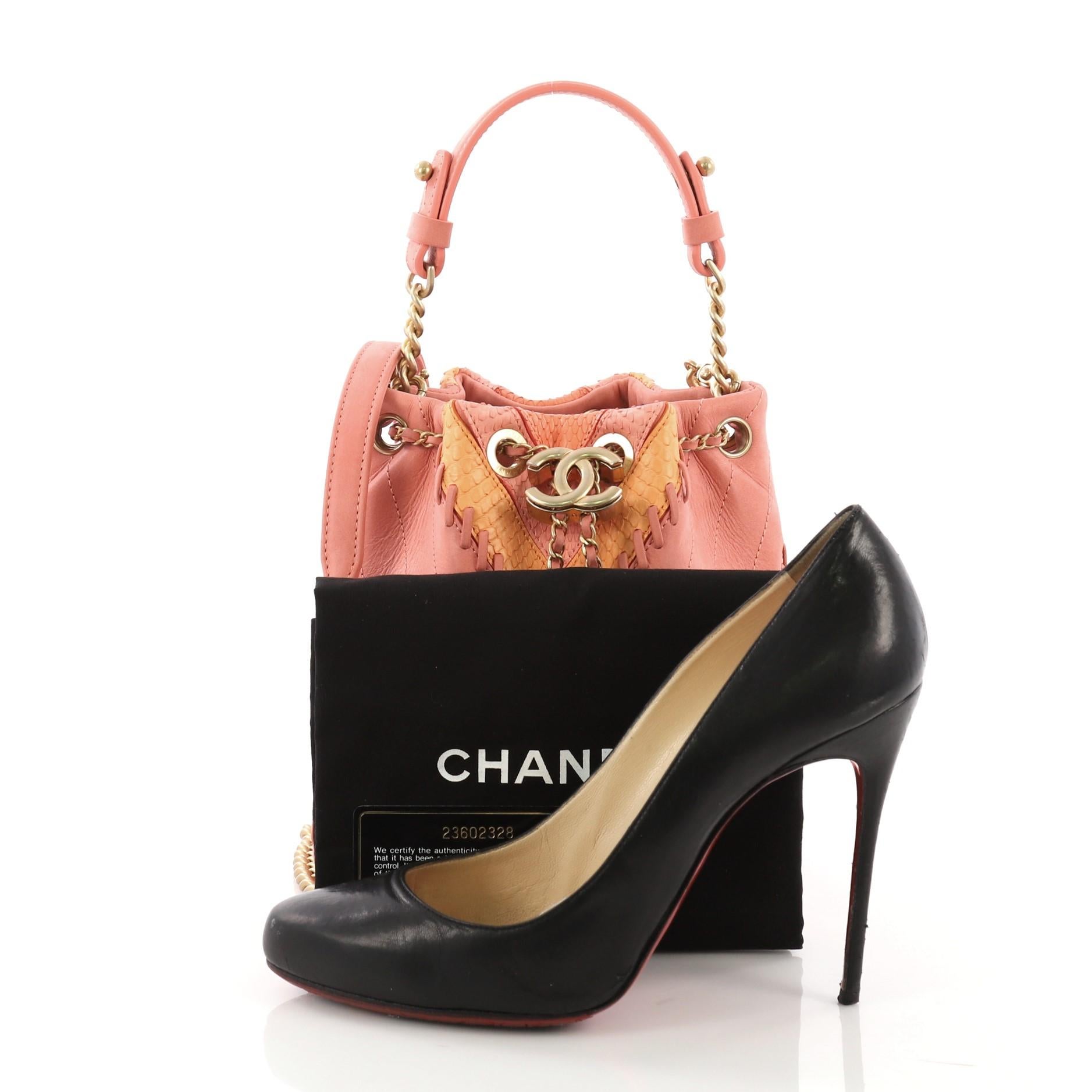 This Chanel CC Drawstring Bucket Bag Whipstitch Chevron Leather and Python Small, crafted from pink whipstitch chevron leather with genuine pink and orange python, features chain link strap with leather pad, interlocking CC logo accent, and matte