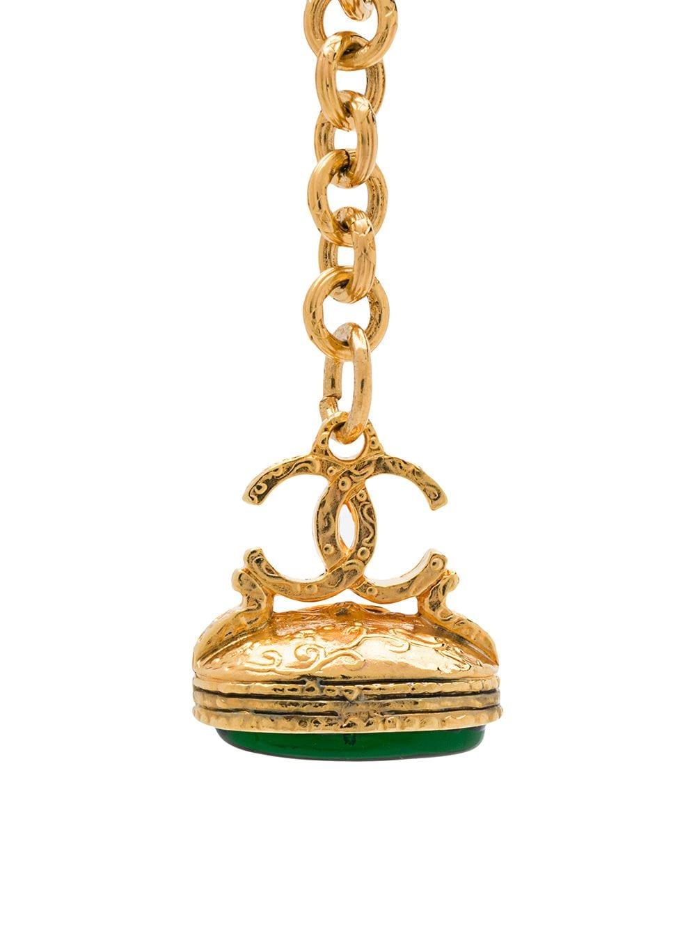 Crafted in France from antique gold plated metal, this elegant keychain boasts a cable-link chain, an engraved finish and a green gripoix glass stone embellishment which hangs decoratively underneath the signature interlocking CC logo charm from a