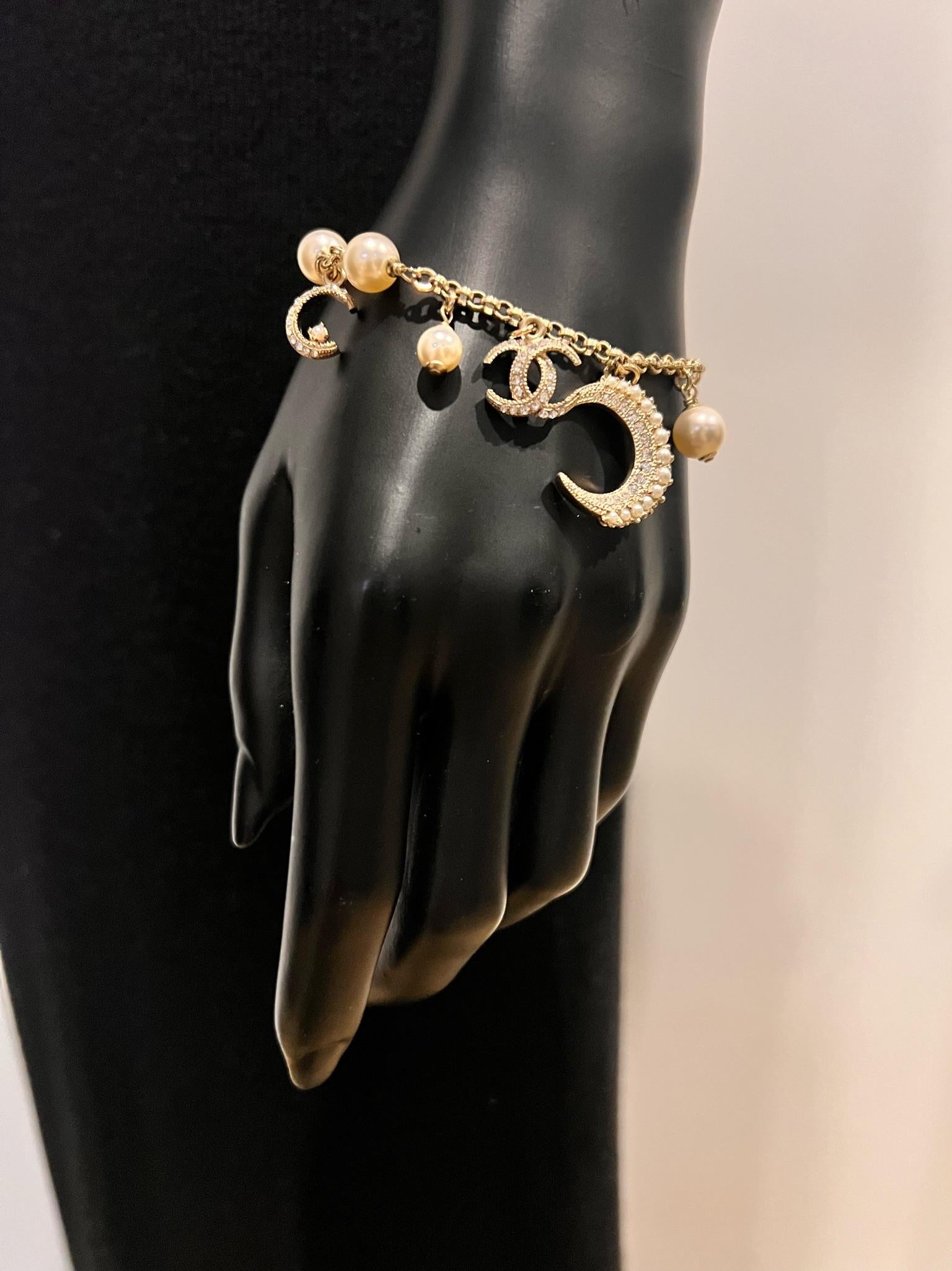 De la collection Cruise 2015. Bracelet à breloques Chanel CC Crescent Moon en métal doré, avec stations en fausses perles et fermoir à mousqueton. Comprend une pochette et une boîte à bijoux. Type de métal : Métal doré
Marques : Signature du