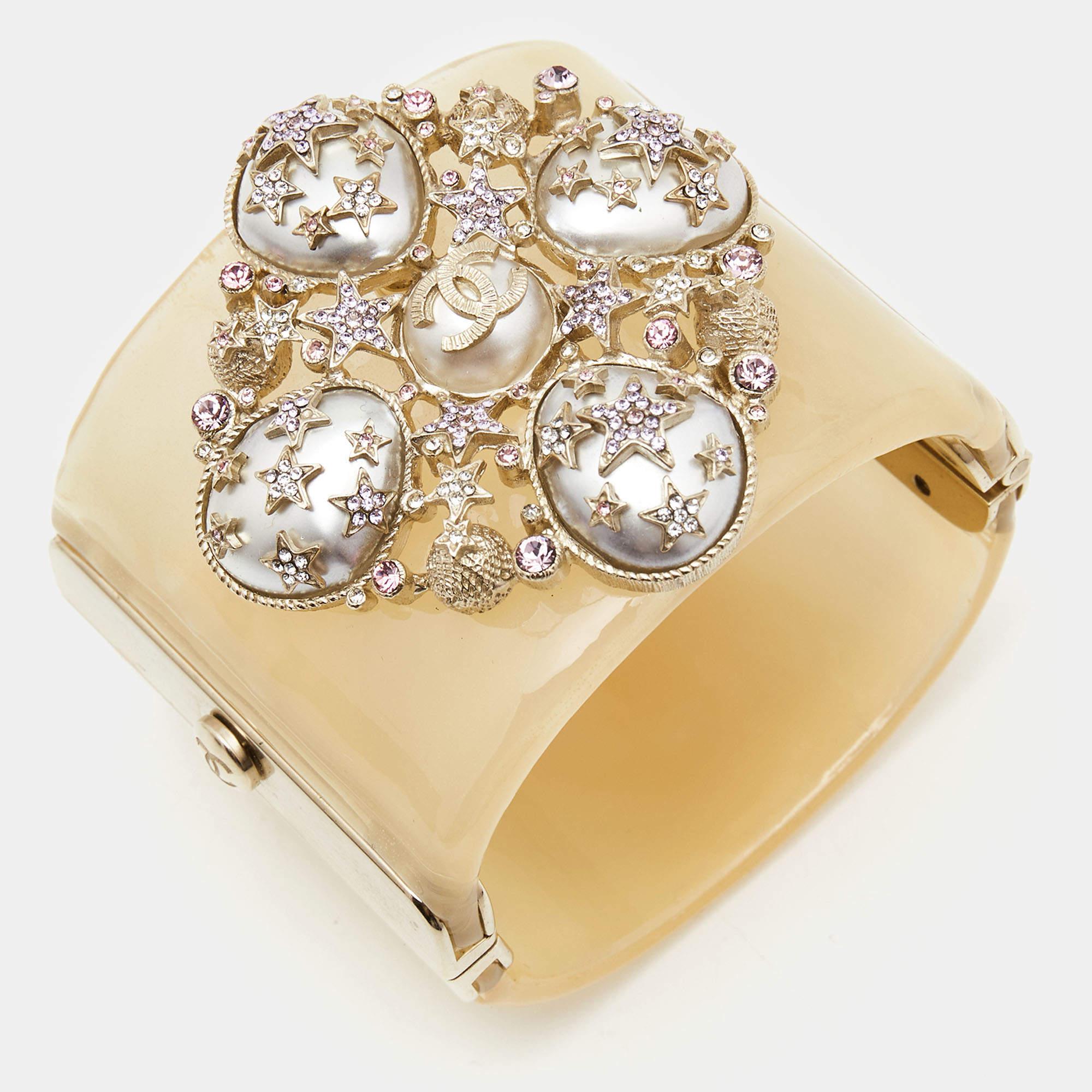 The Chanel CC bracelet is an exquisite accessory. This cuff features the iconic CC logo adorned with faux pearls and crystals, set in a glossy resin base. Its gold-tone finish exudes luxury, making it a statement piece for any elegant ensemble.


