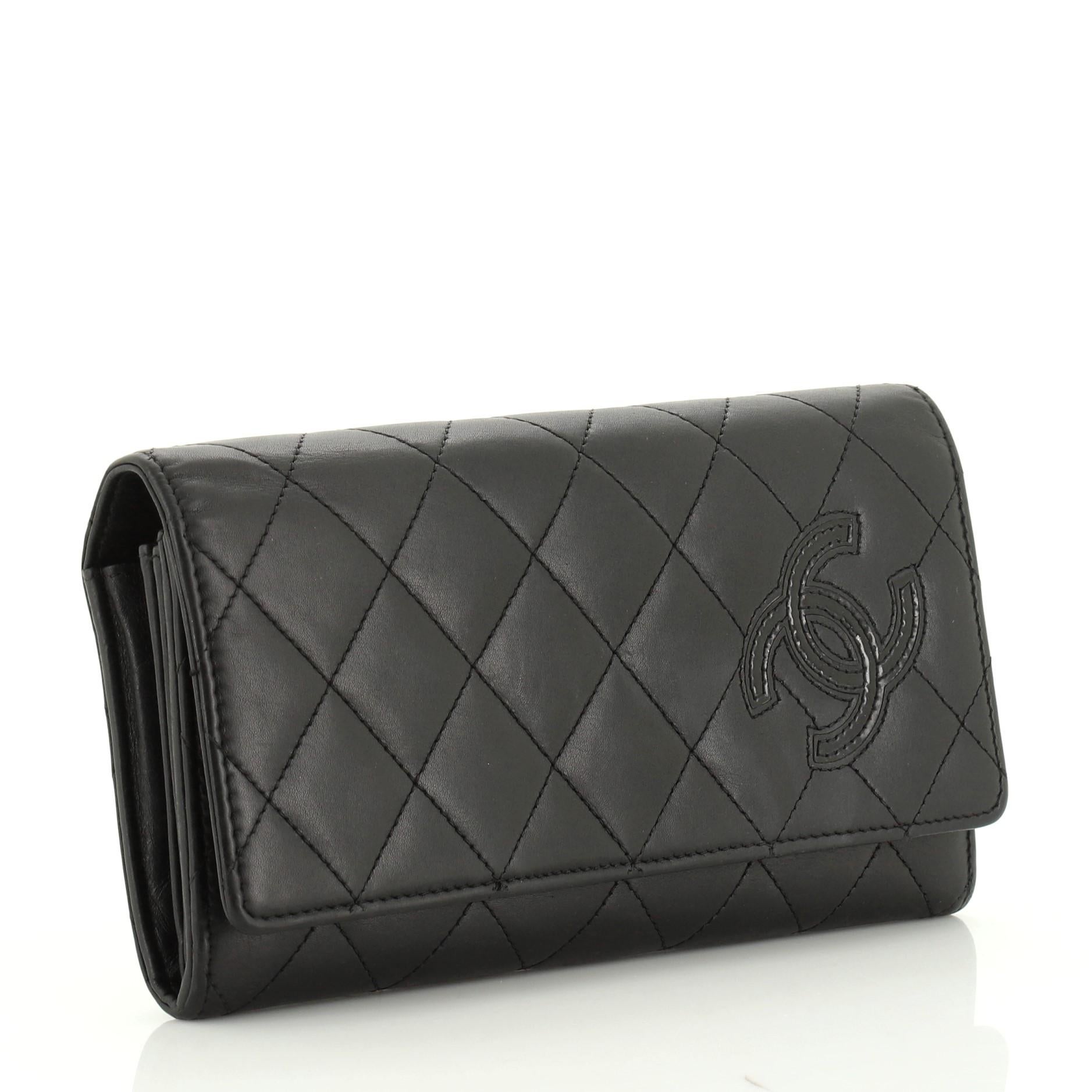 This Chanel CC Flap Wallet Quilted Lambskin Long, crafted in black quilted lambskin leather, features interlocking CC logo, gusseted sides, and silver-tone hardware. Its snap button closure opens to a black leather and fabric interior with multiple