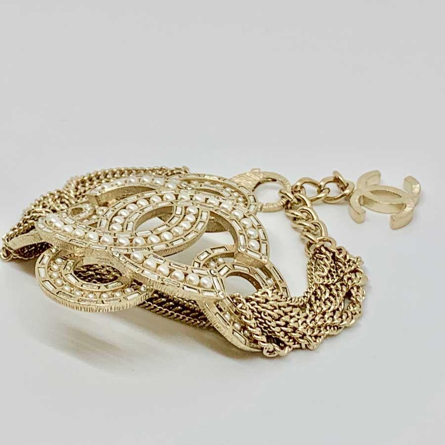 The bracelet comes from Maison CHANEL. It consists of a multi-row golden chain with a CC set with pearls as its central element. Another golden CC hangs at the end of the chain. For a sophisticated and elegant wrist.
The jewel is in very good