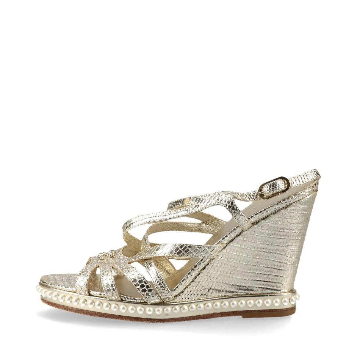 La sandalia de cuña Chanel CC Logo Moc Lizard en dorado es una pieza de lujo que combina una textura exótica con un diseño elegante. Confeccionadas en piel de lagarto repujada de primera calidad, las sandalias presentan un acabado dorado brillante
