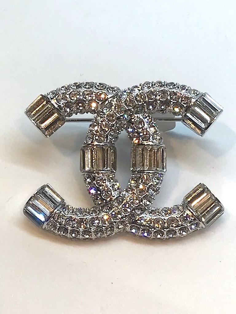 An iconic Chanel interlocking CC logo pin in pave' rhinestones. The end of each letter C and in the middle are beautifully set with baguette rhinestones to compliment the small round pave' set ones. Palladium silver tone body. Pin measures 2