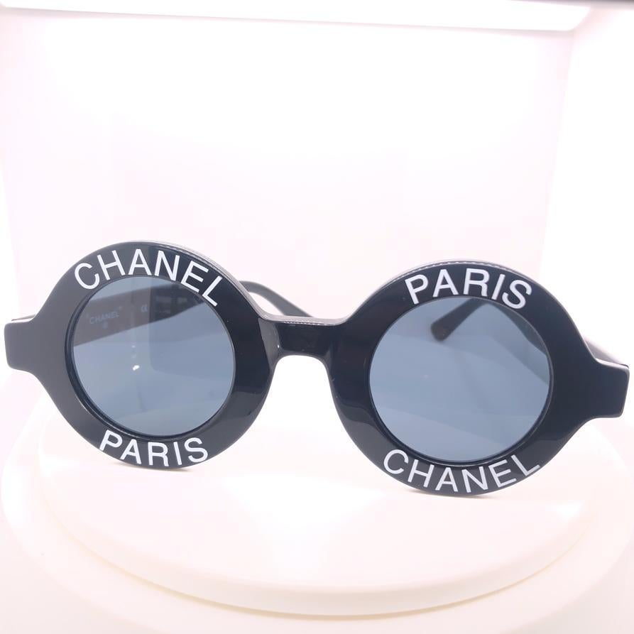 Véritables déclarations de mode, les lunettes de Chanel oscillent entre innovation contemporaine et sophistication classique, comme seule la Maison française sait le faire. Fabriquées en plastique noir, ces lunettes de soleil CC logos présentent une