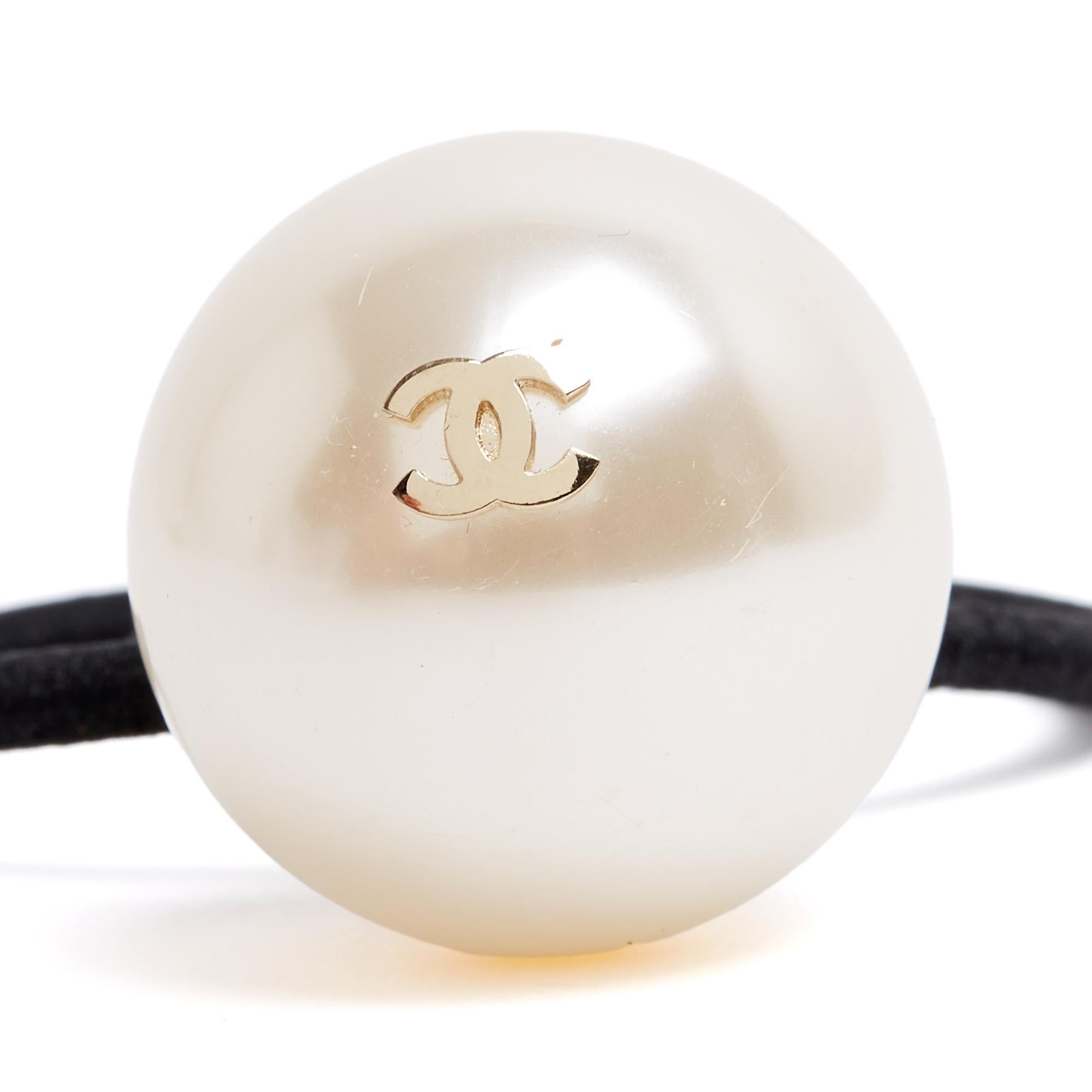 Accessorio elastico per capelli Chanel ornato da un'enorme perla fantasia sormontata da un logo CC placcato oro. Diametro della perla 2,9 cm. L'accessorio è in ottime condizioni, molto luminoso quando viene indossato.
