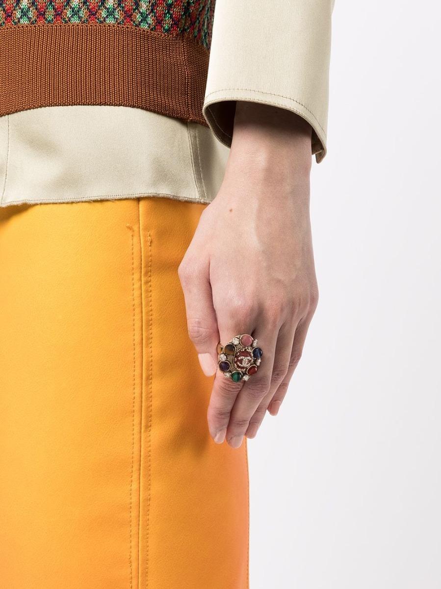 Inspiriert von der Kamelienblüte, einem Symbol von Chanel, zeigt dieser Ring aus zweiter Hand einen wunderschönen roten Stein in der Mitte, der von farbigen Steinen und Strasssteinen umgeben ist und auf einem goldfarbenen Band ruht. Das Modell ist