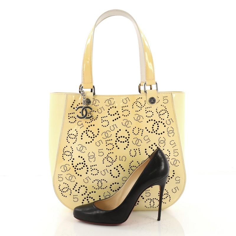 This Chanel CC No.5 Shopping Tote Perforated Patent Medium, crafted in yellow patent leather with perforated Chanel CC logos and lucky number 5, features dual sturdy patent leather handles embellished with small Chanel CC studs, silver CC charm,
