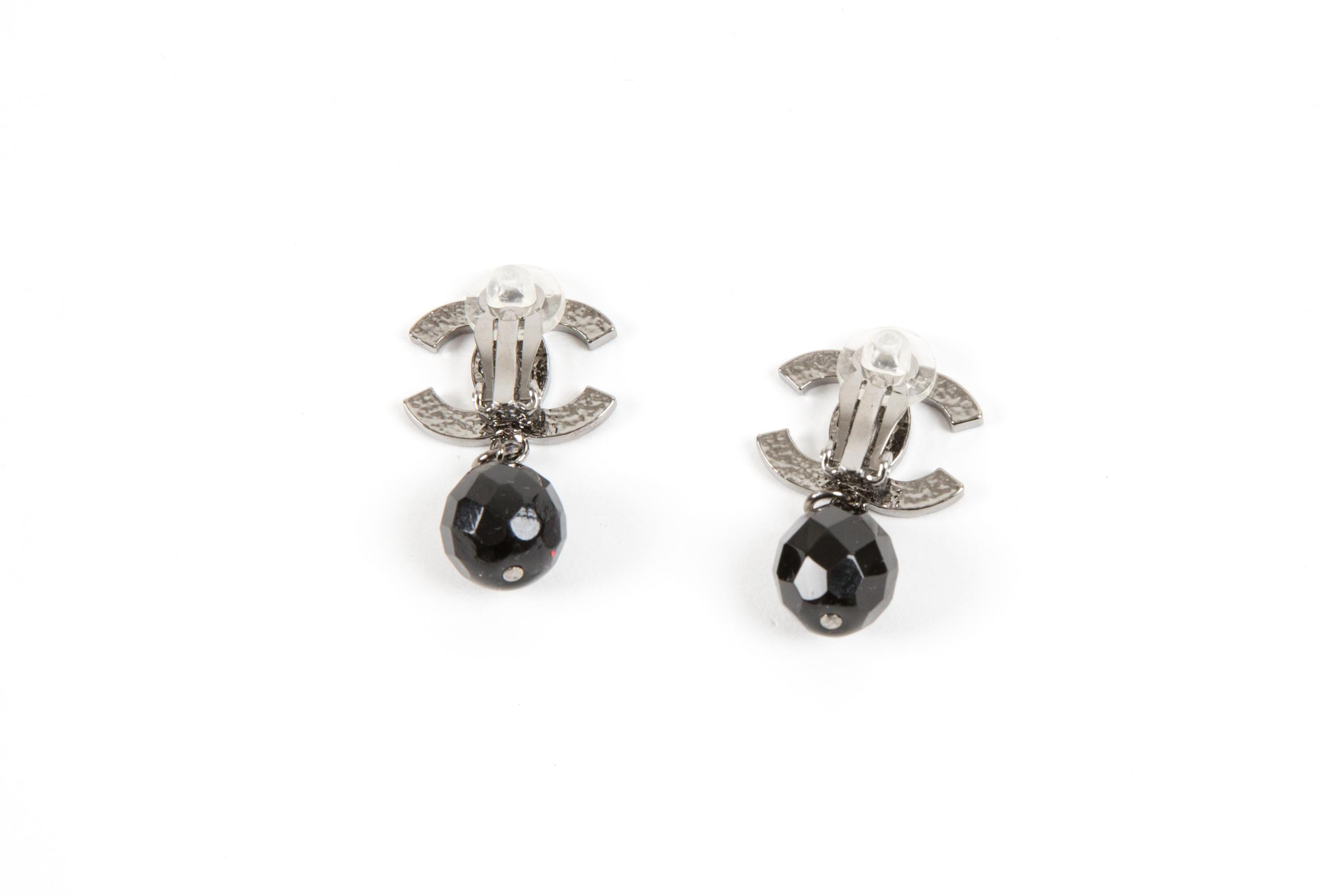 Chanel CC black pendant bead clip-on earrings featuring large logo silver-tone “CC”, a signature interlocking CC logo, back plaque pitted, clip-on design.
They come as a pair. 
Circa 2010  
Good vintage condition. Made in France.  
Length: 1.30in.
