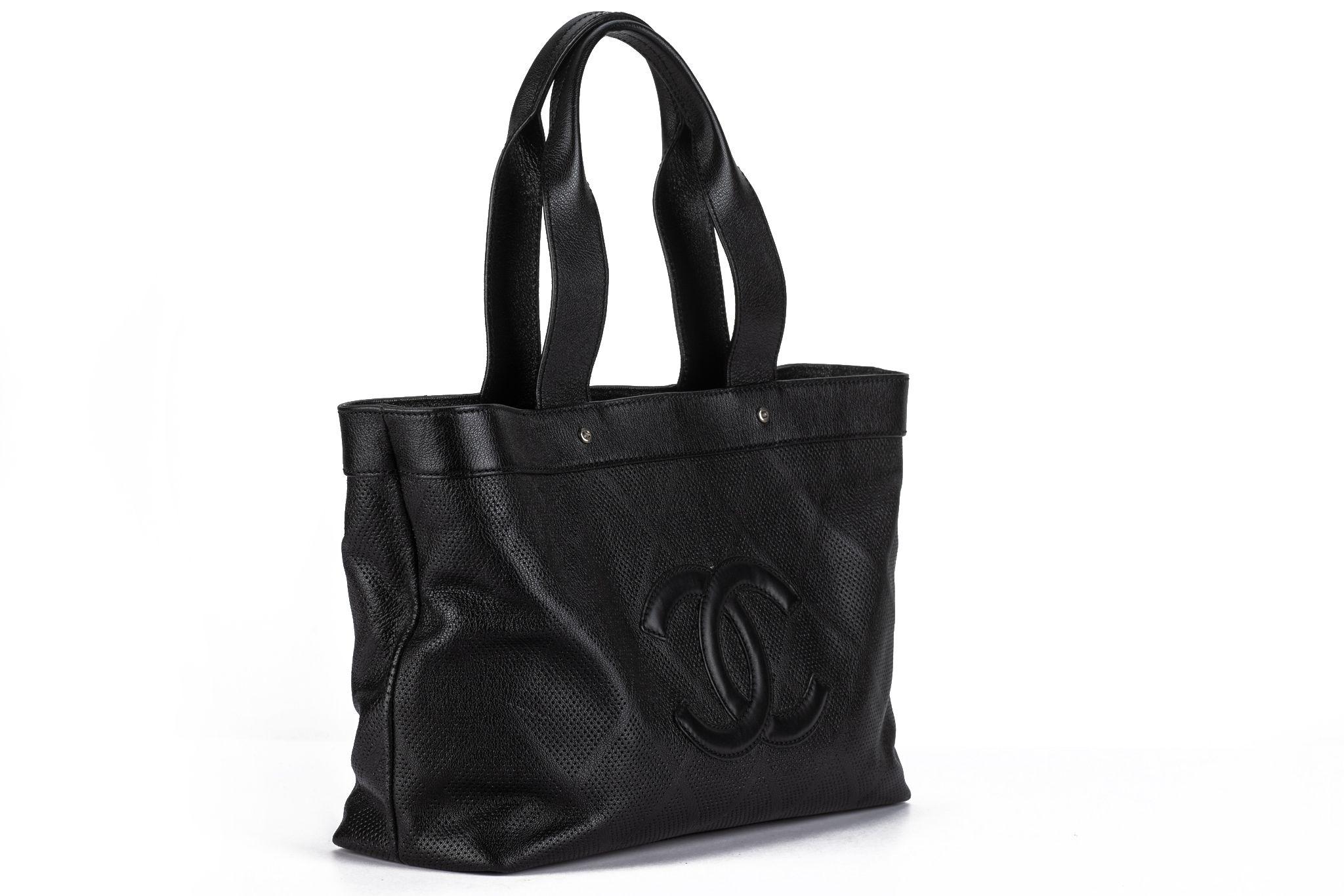 This Chanel leather perforated large CC Tote in black. The tote is a classic, distinctively structured bag that is crafted of stylish black diamond pattern perforated leather. The bag also features two tall leather strap top handles. Comes with