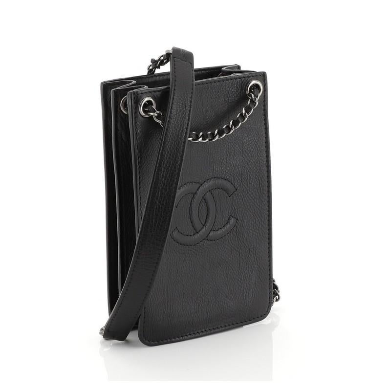 This Chanel CC Phone Holder Crossbody Bag Calfskin, crafted in black calfskin leather, features woven-in leather chain strap with leather pad, front stitched CC detail, expandable sides, and aged silver-tone hardware. It opens to a black fabric