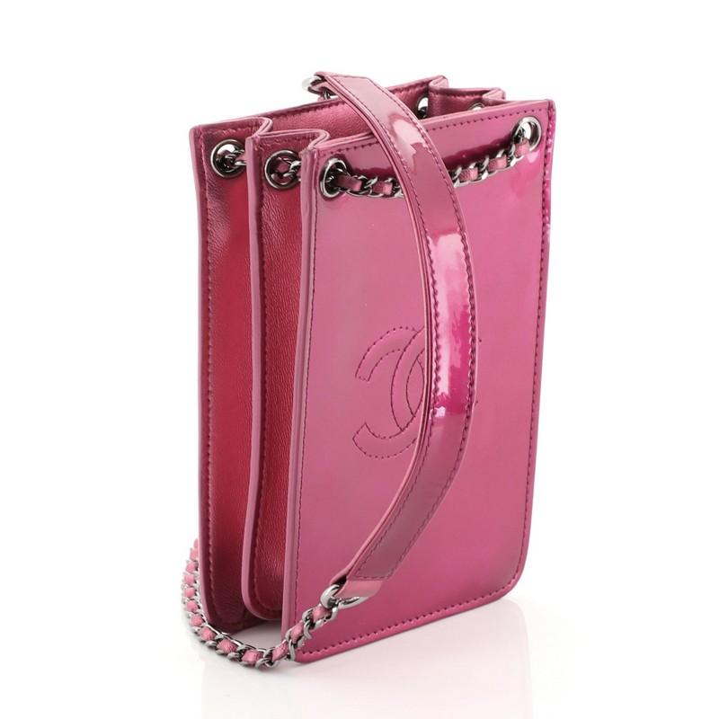 This Chanel CC Phone Holder Crossbody Bag Patent, crafted in pink patent leather, features woven-in leather chain strap with leather pad, front stitched CC detail, expandable sides, and gunmetal-tone hardware. It opens to a black fabric interior.