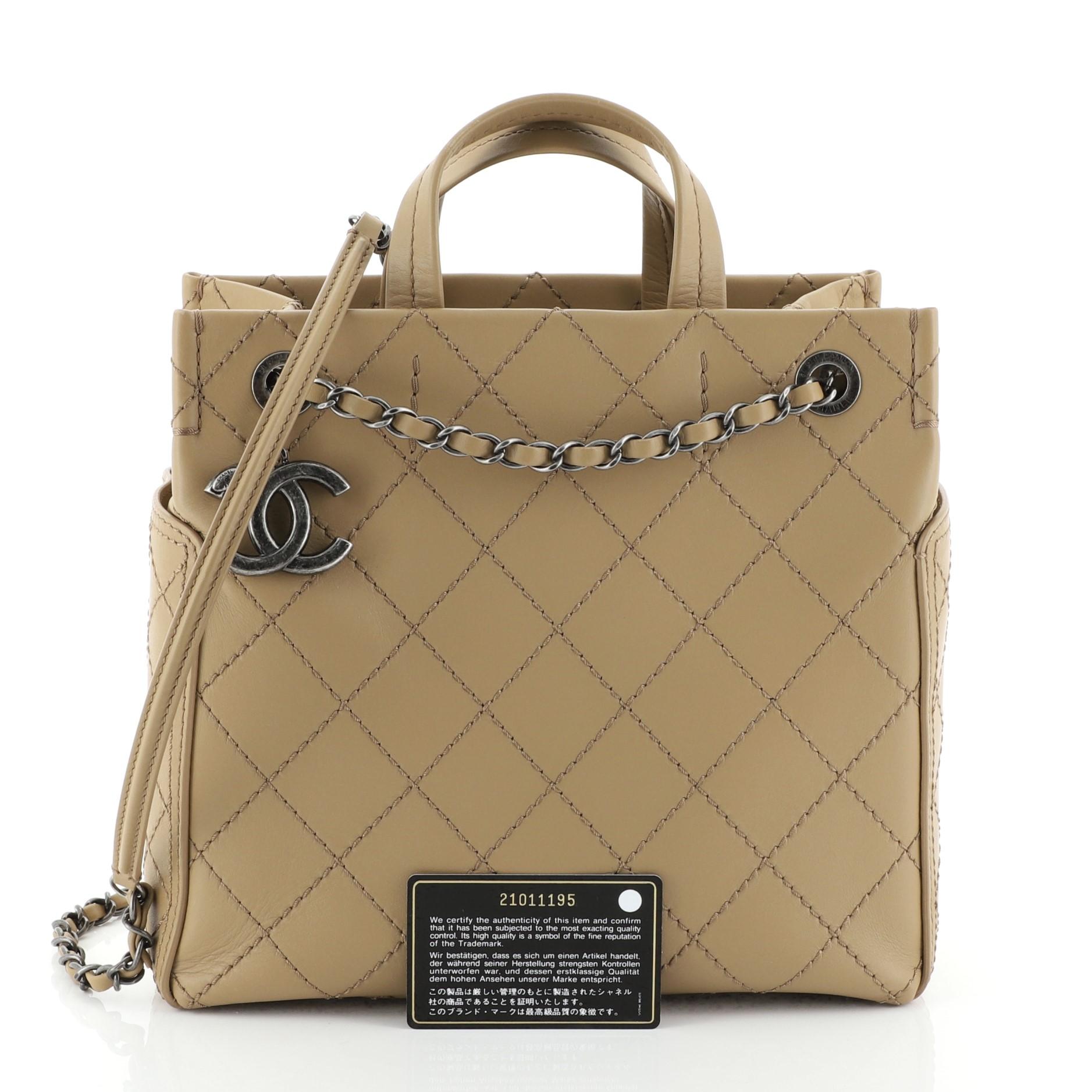This Chanel CC Pocket Tote Quilted Calfskin Small, crafted in neutral quilted calfskin leather, features dual top handles, woven-in leather chain straps with leather pads, exterior side pockets, and aged silver-tone hardware. Its wide open top
