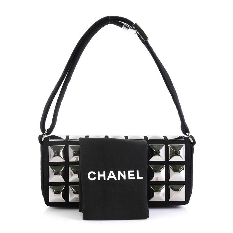 This Chanel CC Pyramid Stud Flap Bag Embellished Jersey, crafted in black jersey, features a full frontal flap with silver diamond shaped studs, jersey top strap and silver-tone hardware. It opens to a black fabric interior with zip pocket. Hologram