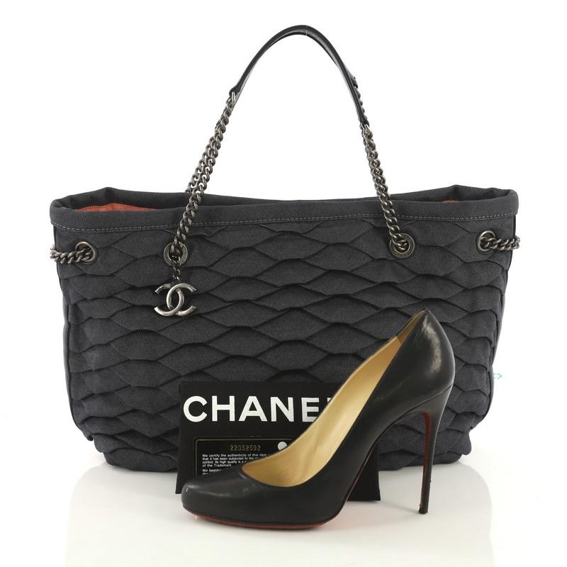 This Chanel CC Shopping Tote Scale Effect Denim Medium, crafted from navy effect denim, features dual chain-link straps with leather pads, protective base studs, and aged silver-tone hardware. Its magnetic snap closure opens to a navy fabric