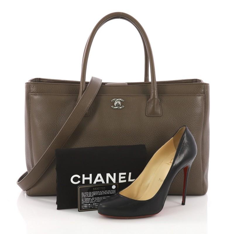 This Chanel Cerf Executive Tote Leather Medium, crafted from brown leather, features dual rolled tall handles, front pocket with CC turn-lock closure, and silver-tone hardware. Its top magnetic snap closure opens to a grey fabric interior with zip
