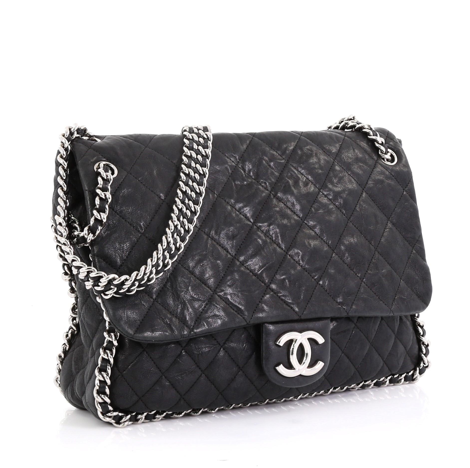 This Chanel Chain Around Flap Bag Quilted Leather Maxi, crafted in black quilted leather, features woven-in leather chain strap, chain-around design, frontal flap with CC logo, and silver-tone hardware. Its magnetic snap closure opens to a gray