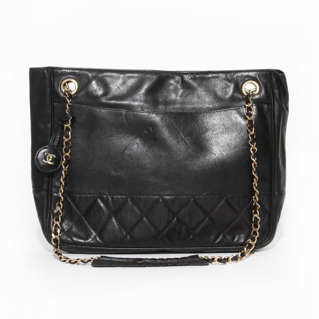 Chain handle tote by Chanel 
Between 1984-1986
Black leather
Gold-tone hardware
Snap closure on front flap
Open top with snap closure 
Quilted leather trim 
Dual leather and chain-link shoulder strap
Two interior zip pockets
Leather CC hanging