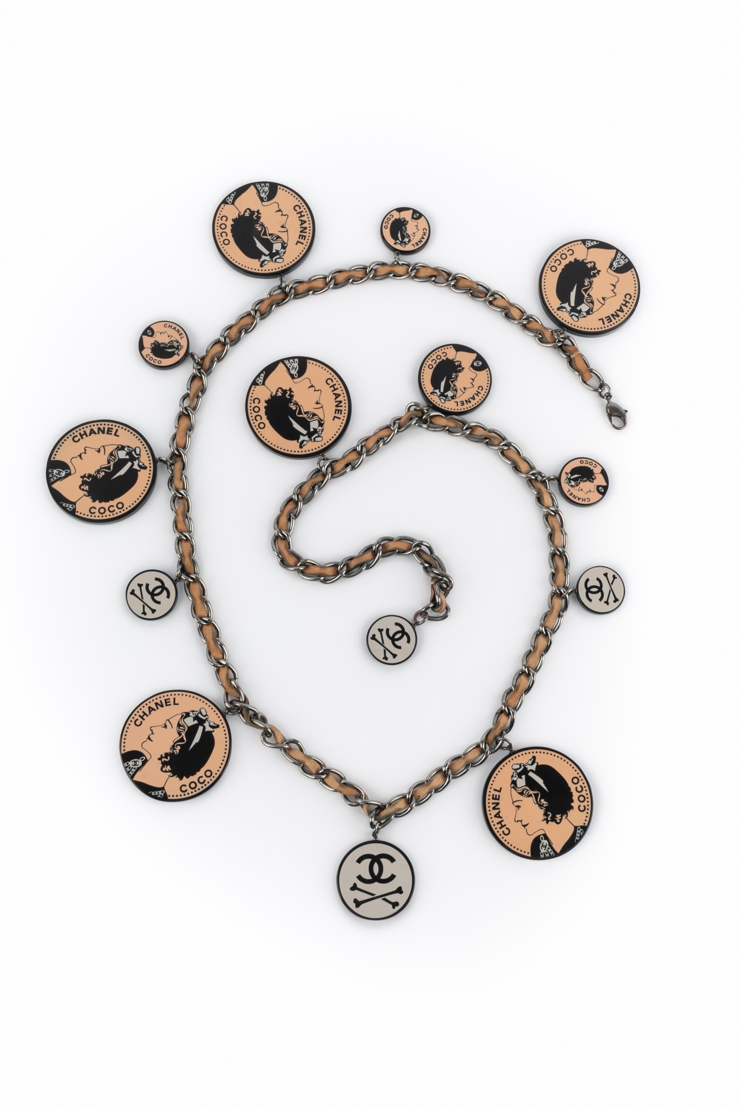 CHANEL - (Fabriqué en France) Collier en métal argenté avec un ruban de cuir couleur corail, des breloques en bakélite noires et couleur corail. Collectional printemps-été 2003 sous la direction artistique de Karl Lagerfeld.

Condit :
Très bon