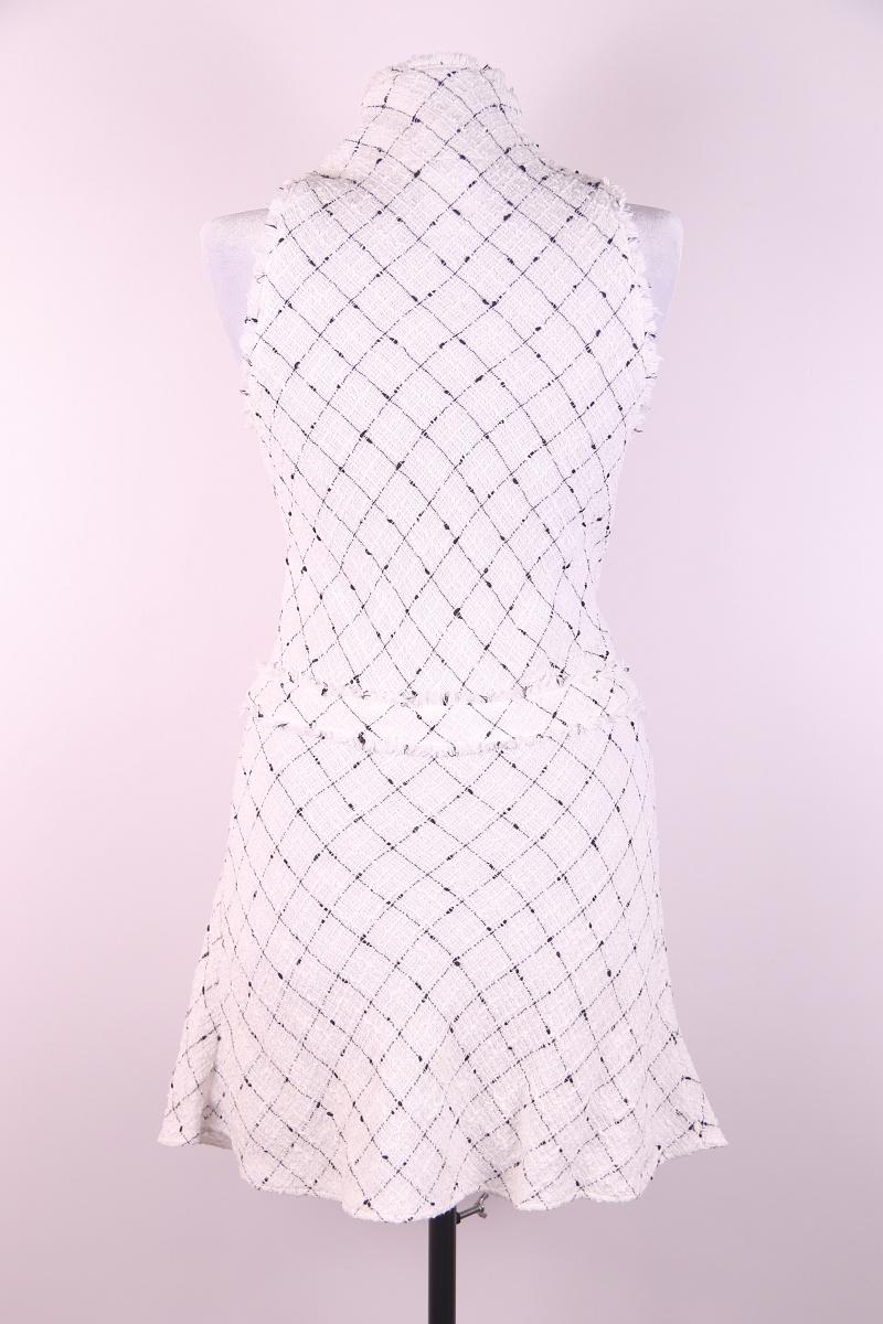 Cette robe de printemps en coton blanc de Chanel présente le tissu tweed emblématique, un modèle sans manches et un col roulé. Il est doté d'une fermeture à glissière sur le devant. La taille tombante présente le bouton logo noir et blanc signature,