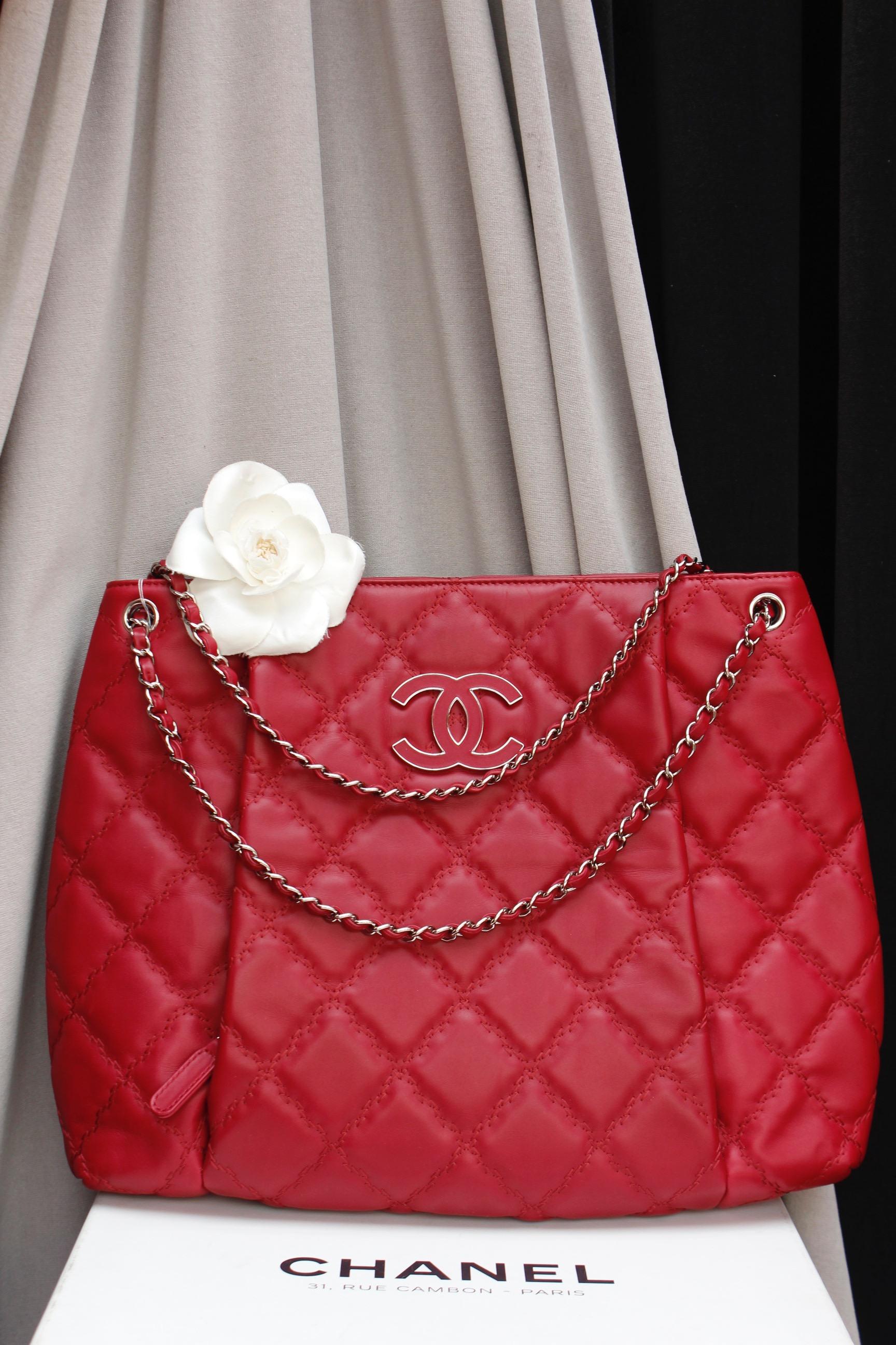 CHANEL (Made in France) Wide tote bag composed of cherry red quilted leather with rounded edges. The front features a zipped pocket decorated with a silver plated and tonal leather CC logo. The silver plated handle is entwined with red leather.

The