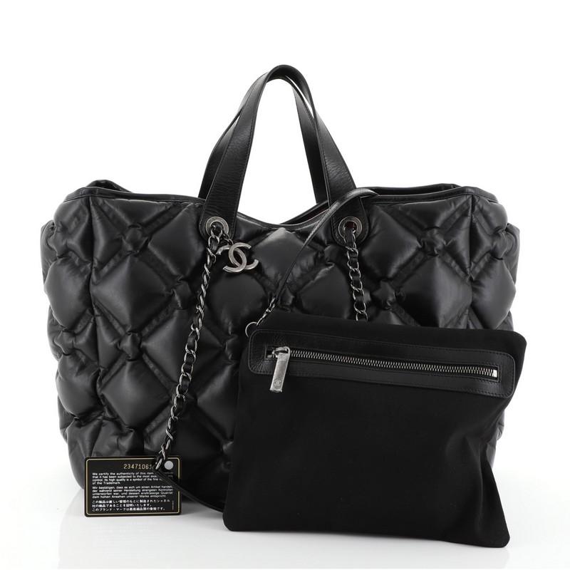 This Chanel Chesterfield Shopping Tote Quilted Leather Large, crafted in black quilted leather, features dual top leather handles, woven-in leather chain link straps, protective base studs, and aged silver-tone hardware. It opens to a red nylon