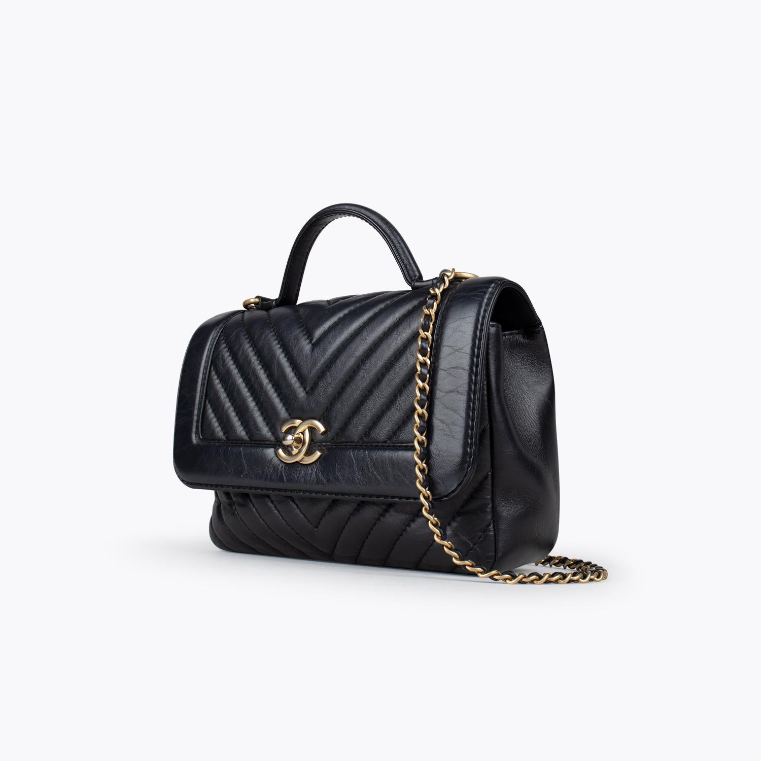 Chanel Chevron Top Handle Flap Bag

- Black Leather
- Antiqued Gold-Tone Hardware
- Flat Handle & Chain-Link Shoulder Strap
- Chain-Link Accents & Single Exterior Pocket
- Grosgrain Lining & Single Interior Pocket
- Turn-Lock Closure at